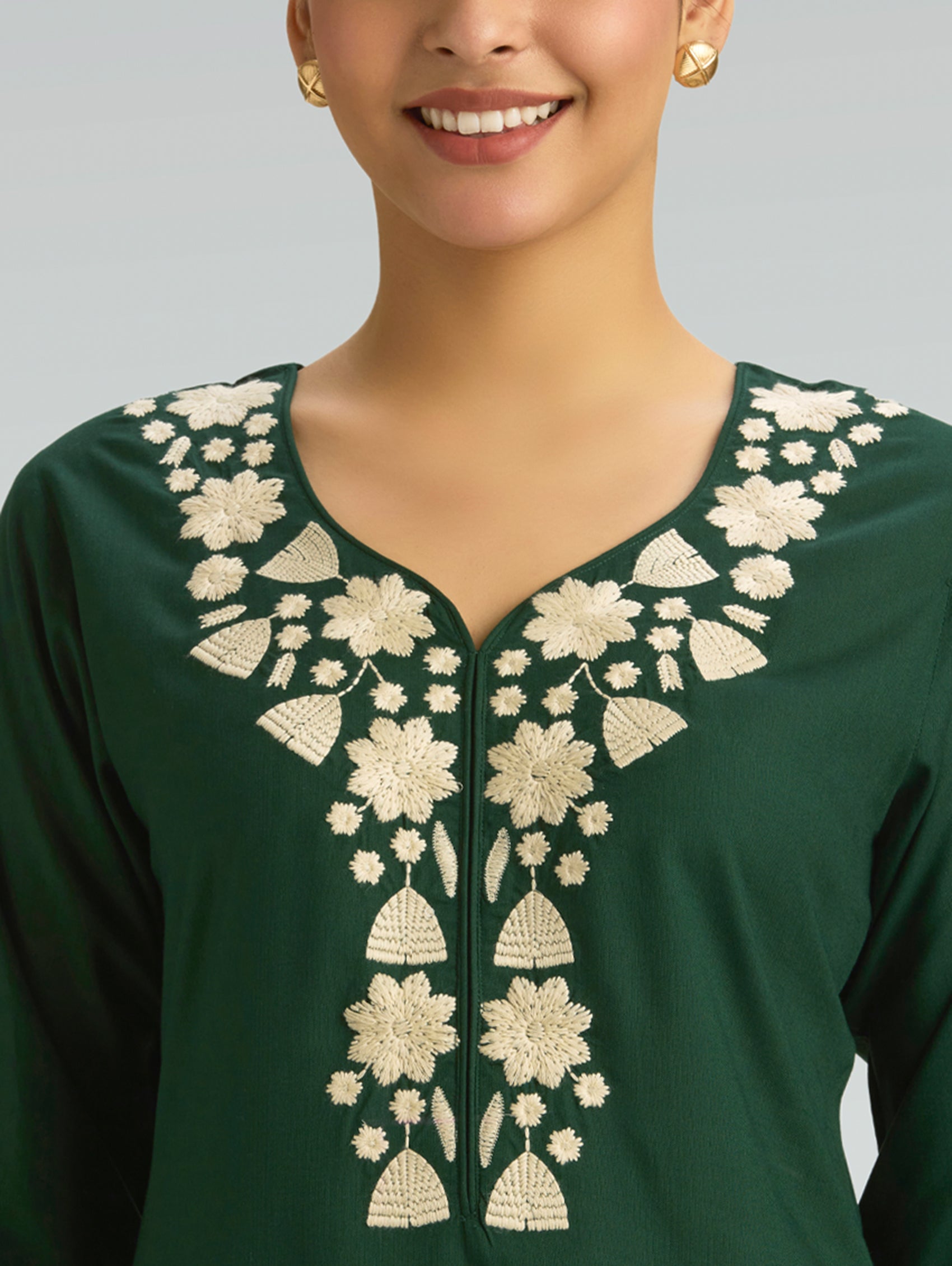 Green traditional outfit with white floral embroidery on a neutral background