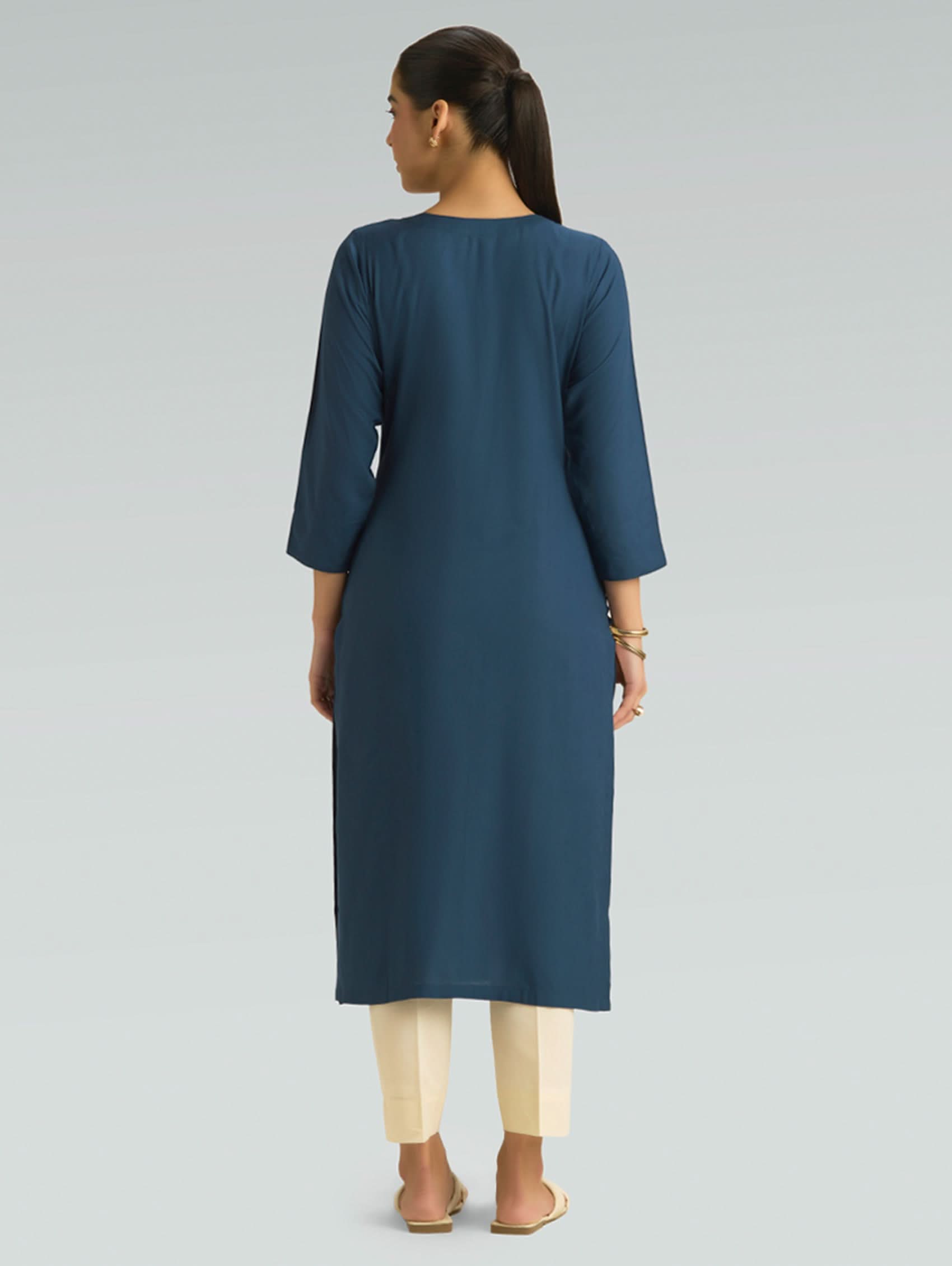 “A woman wearing a blue kurta with beige pants, shown from the back against a gray background.”