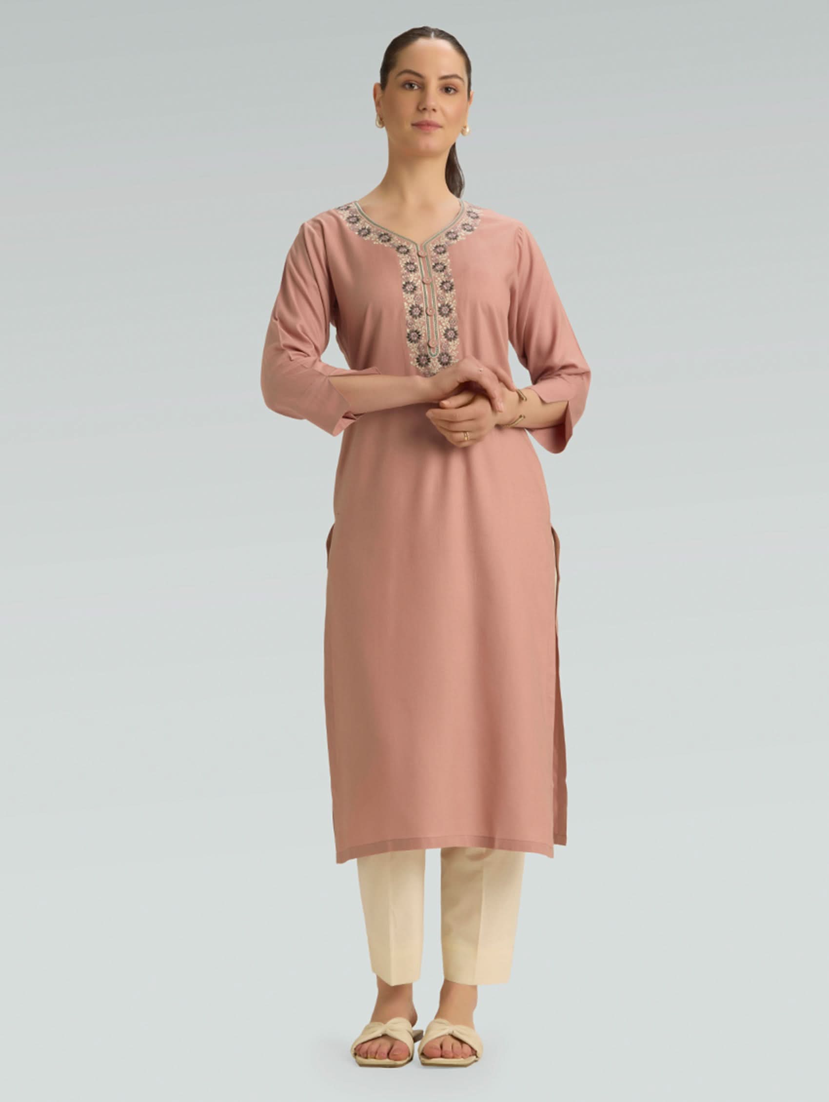 Woman wearing a pink kurta with intricate embroidery on a gray background
