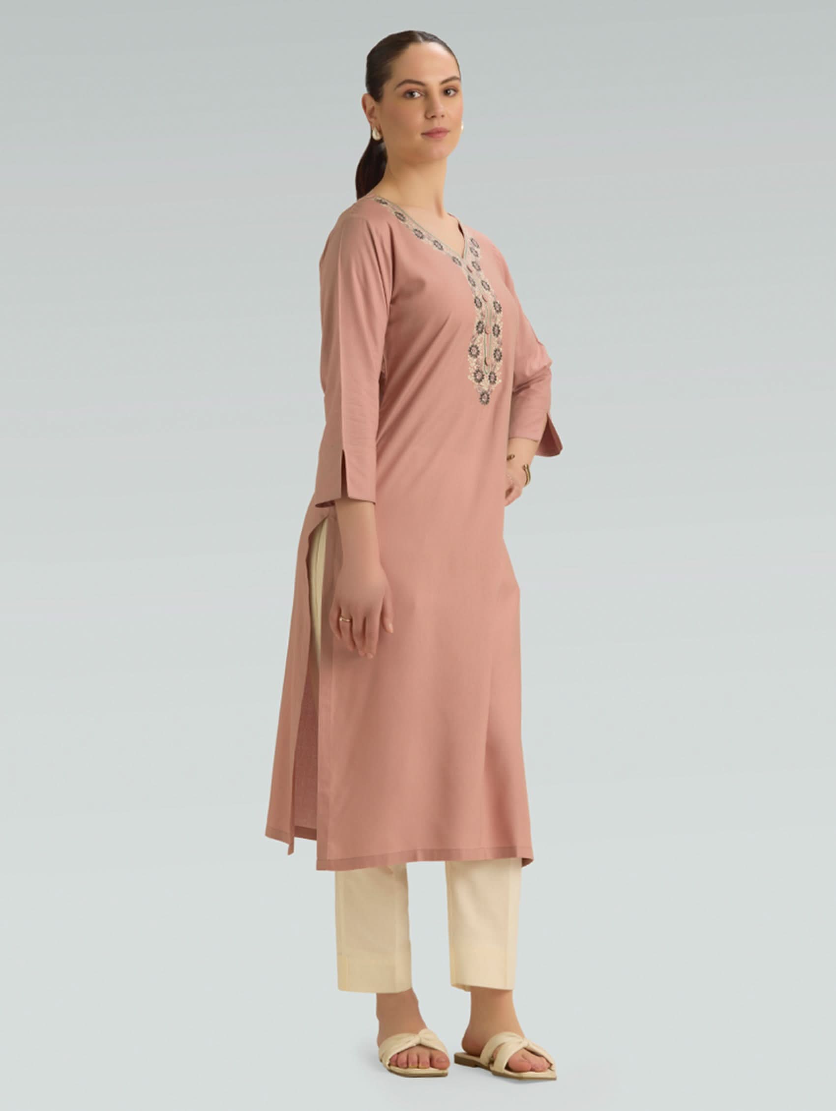 Woman wearing a long, light brown dress with a matching cardigan on a gray background