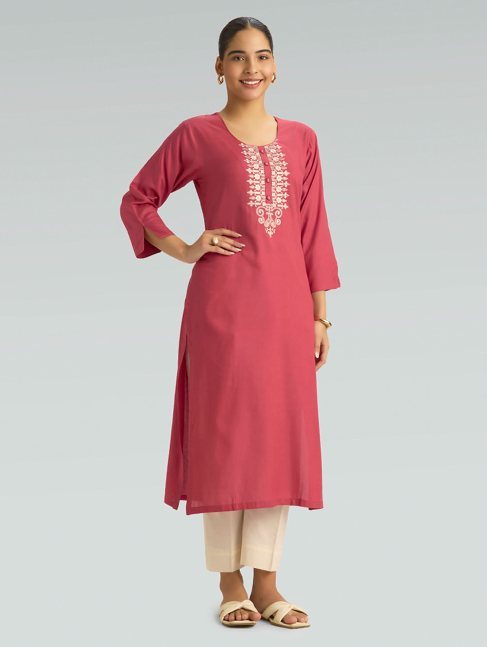 A woman wearing a straight-fit pink kurta with a round neckline, adorned with computerized thread embroidery, set against a soft gray background.