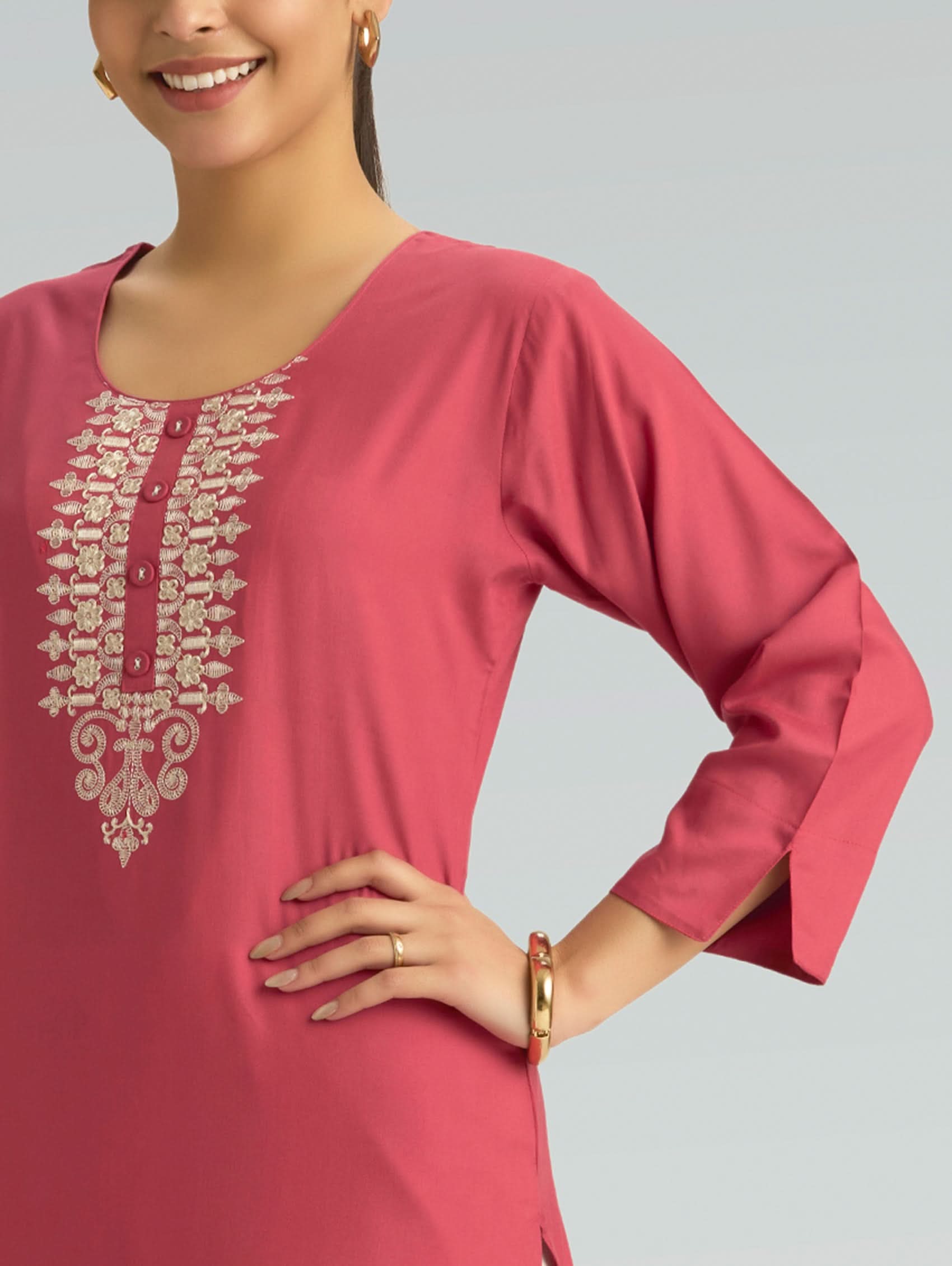 A woman wearing a straight-fit pink kurta with a round neckline, adorned with computerized thread embroidery, set against a soft gray background.