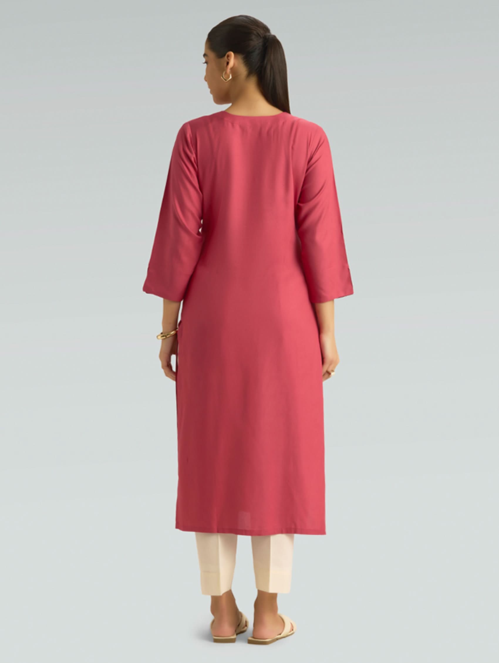A woman in a straight-fit pink kurta with a round neckline, adorned with computerized thread embroidery, shown in a back pose against a soft gray background.