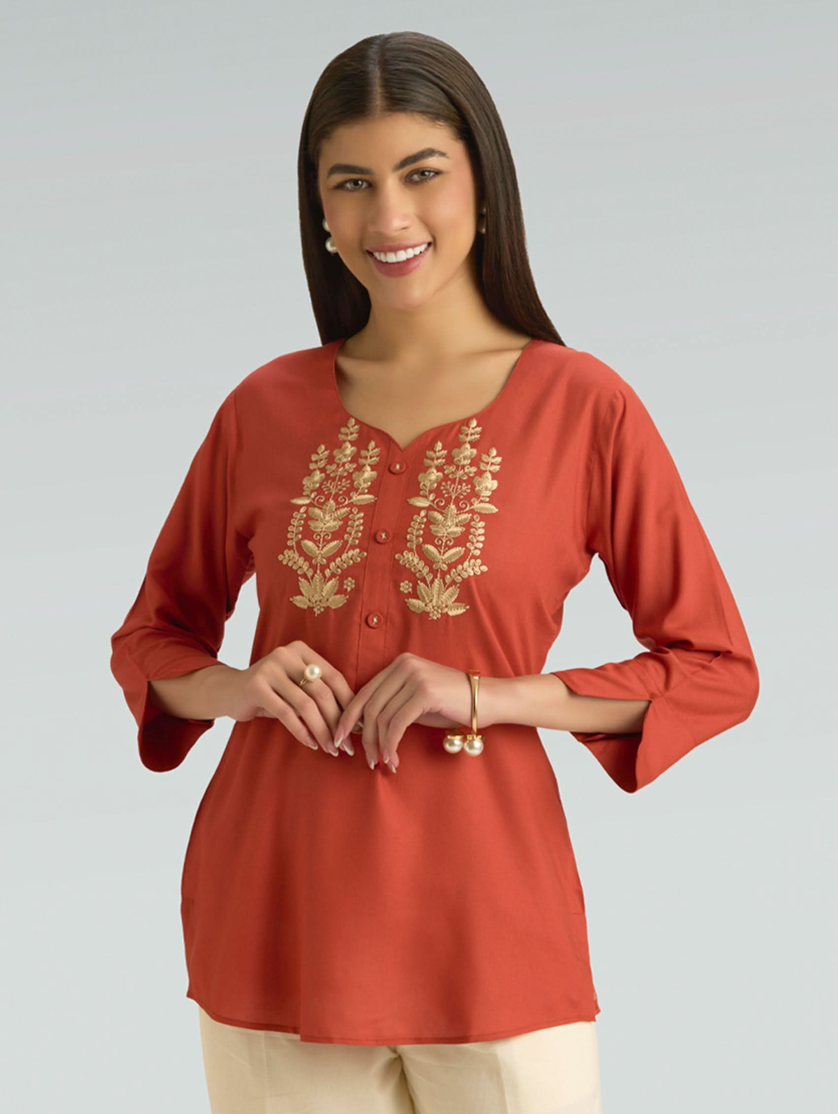 Woman wearing a red kurta with gold embroidery on a gray background