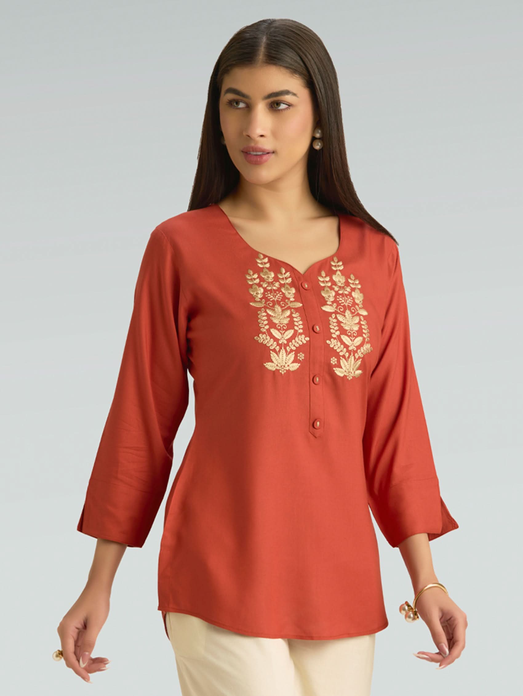 Woman wearing a red embroidered top against a gray background