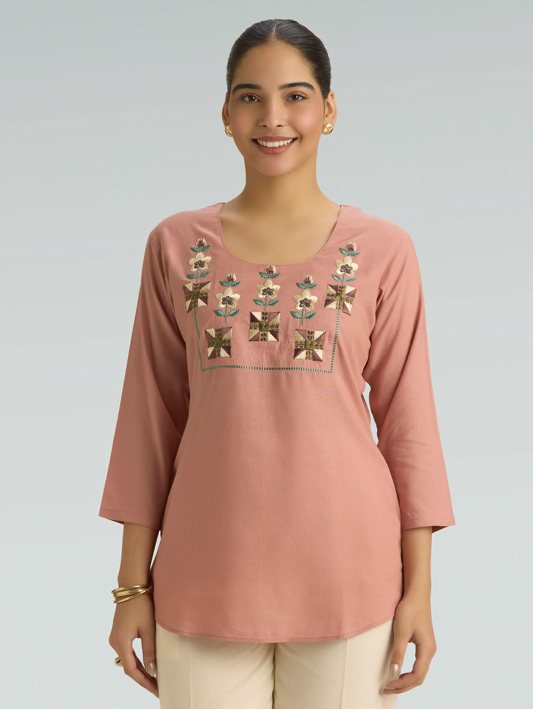 Woman wearing a pink top with floral embroidery on a gray background