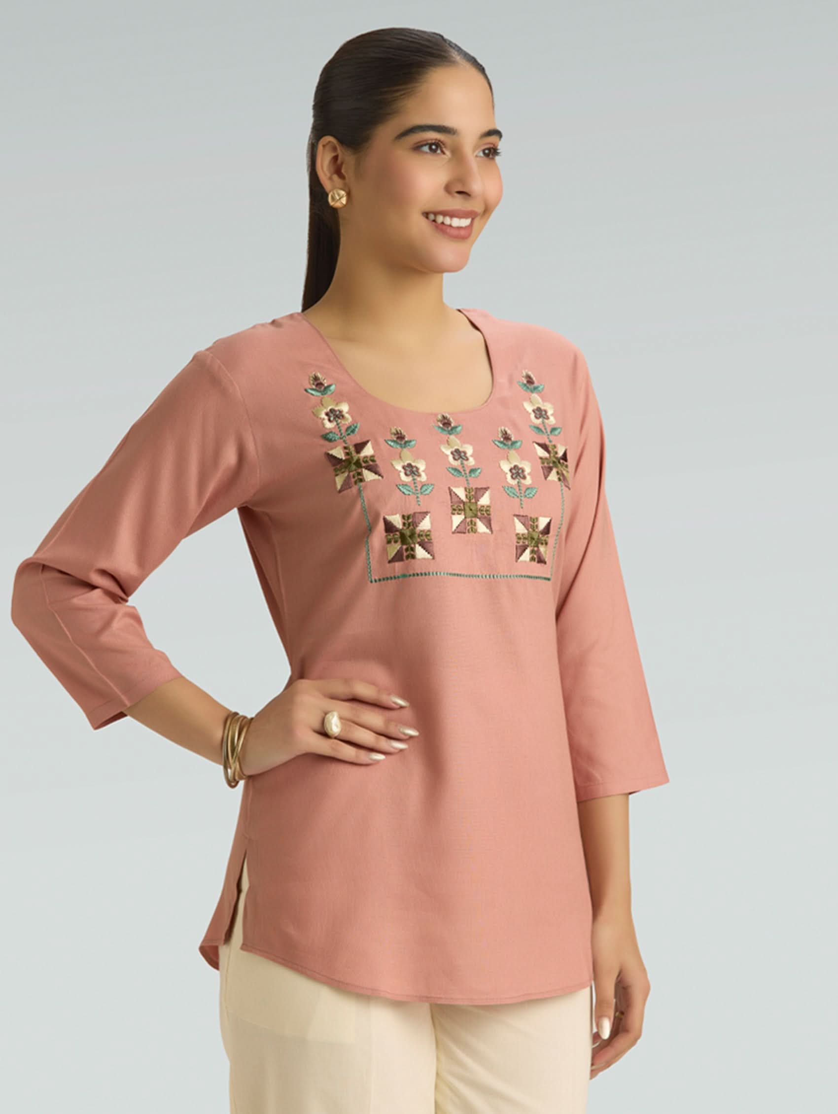 Woman wearing a pink embroidered top on a gray background