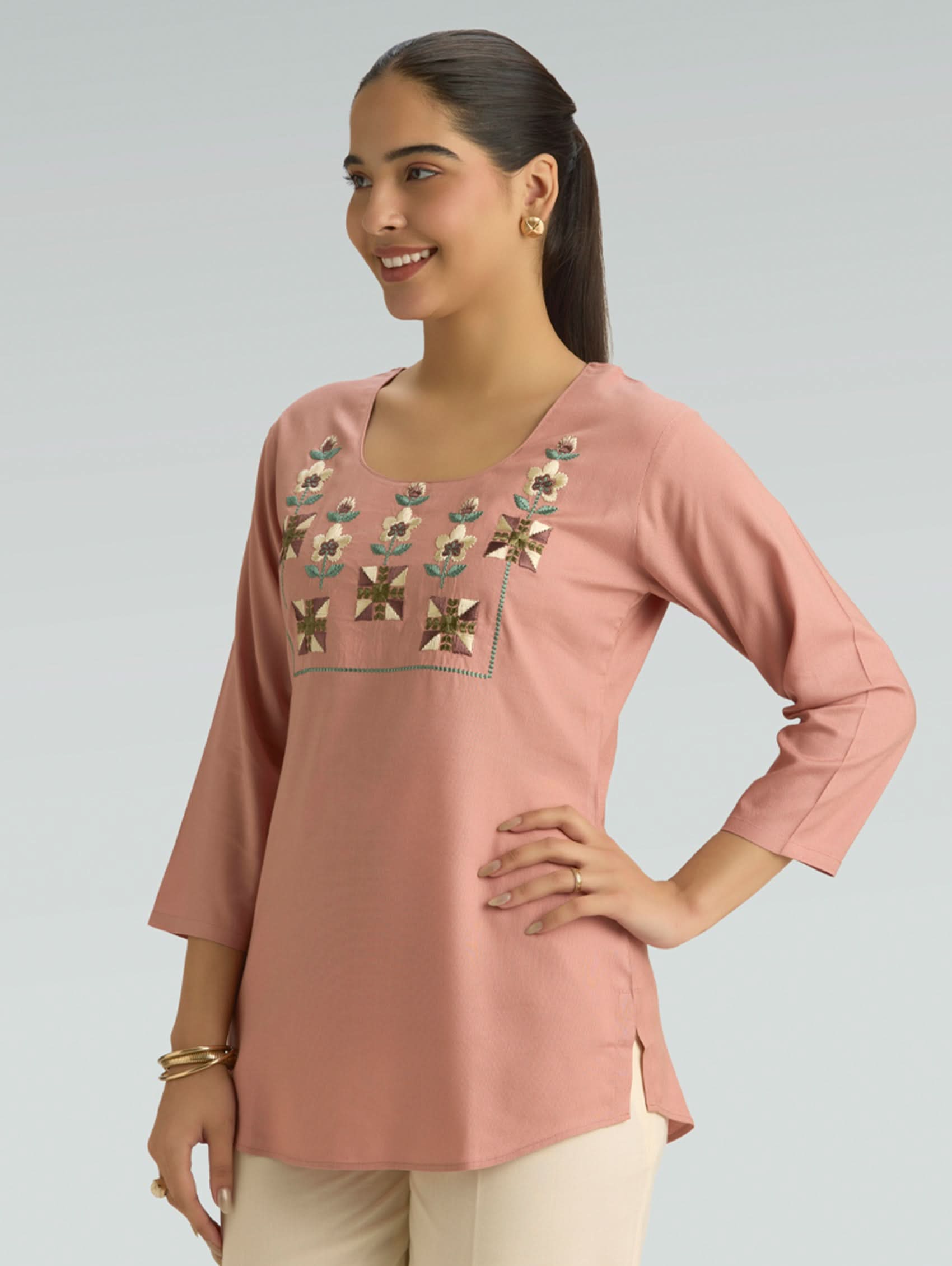 Woman wearing a pink embroidered top against a gray background