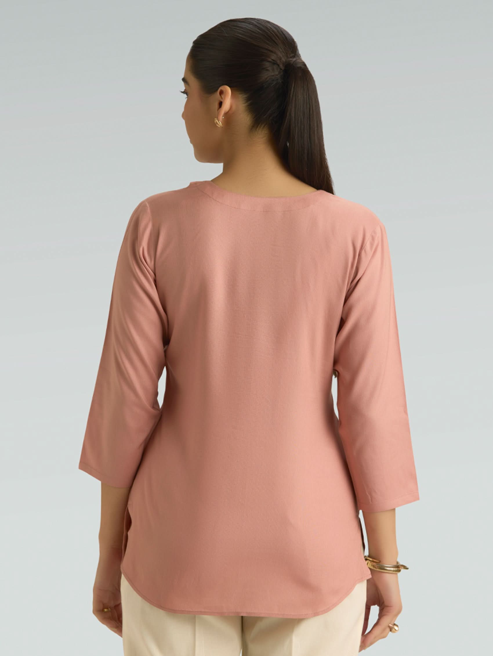 Woman wearing a pink long-sleeve top against a gray background