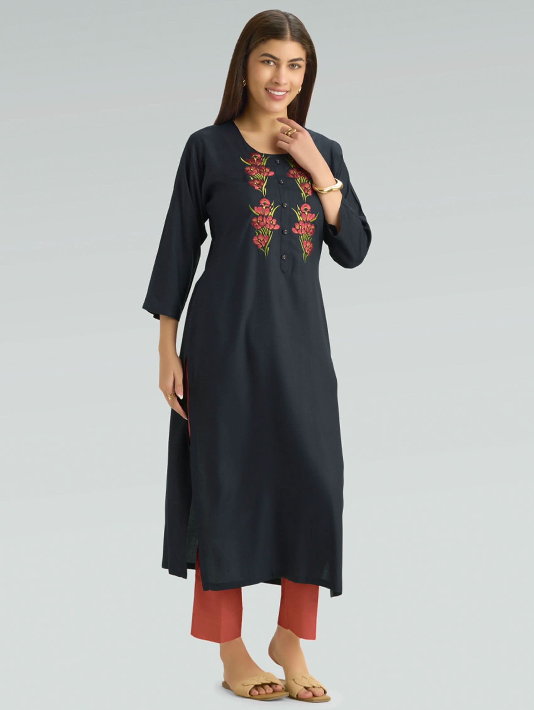 Woman wearing a black kurta with red floral embroidery on a gray background