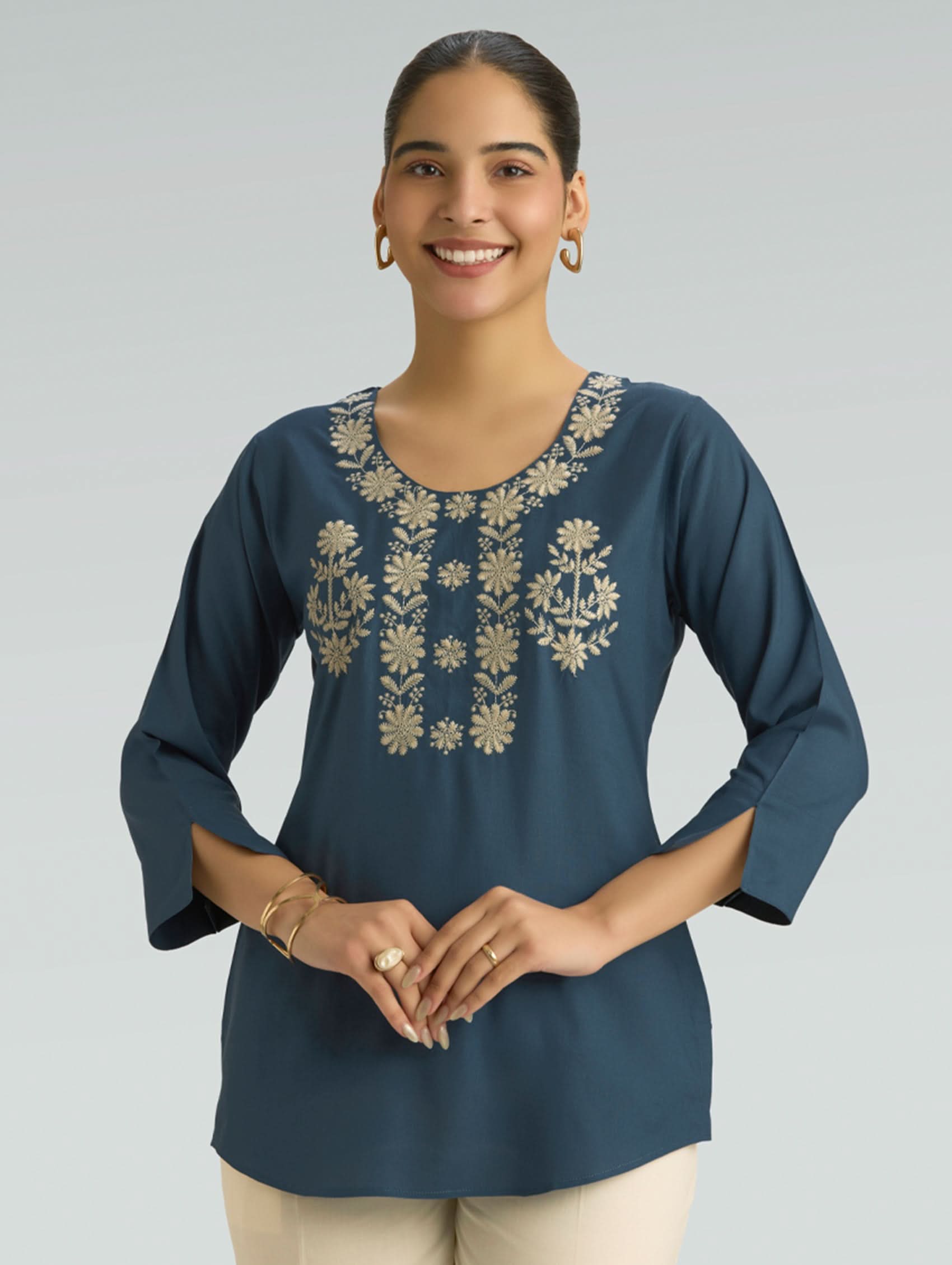 Woman wearing a blue embroidered top against a gray background