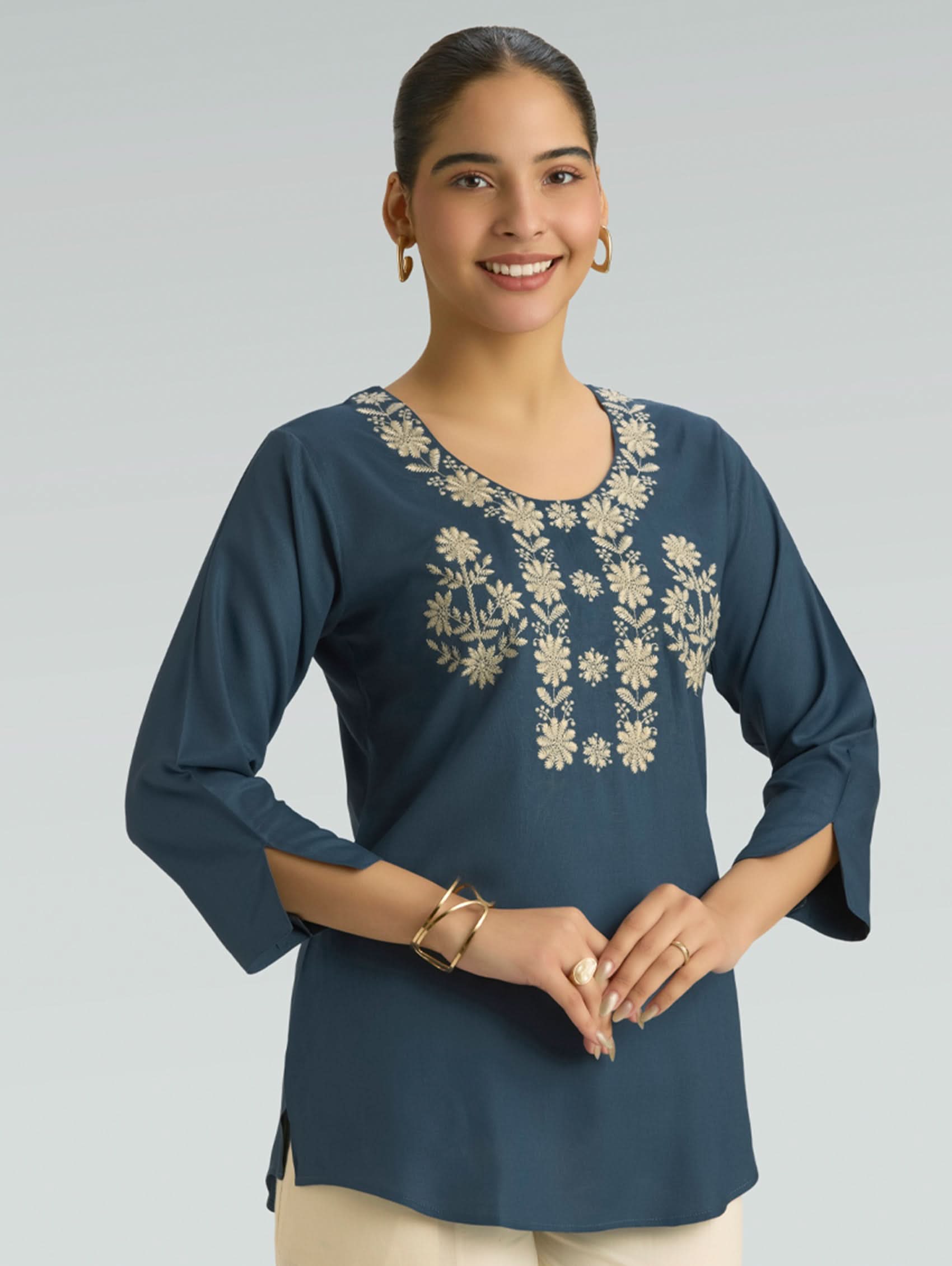 Woman wearing a blue embroidered top on a gray background