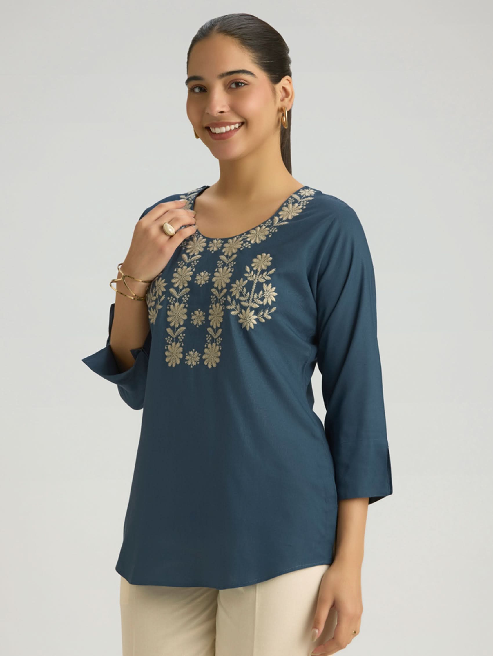 Woman wearing a blue embroidered top on a plain background