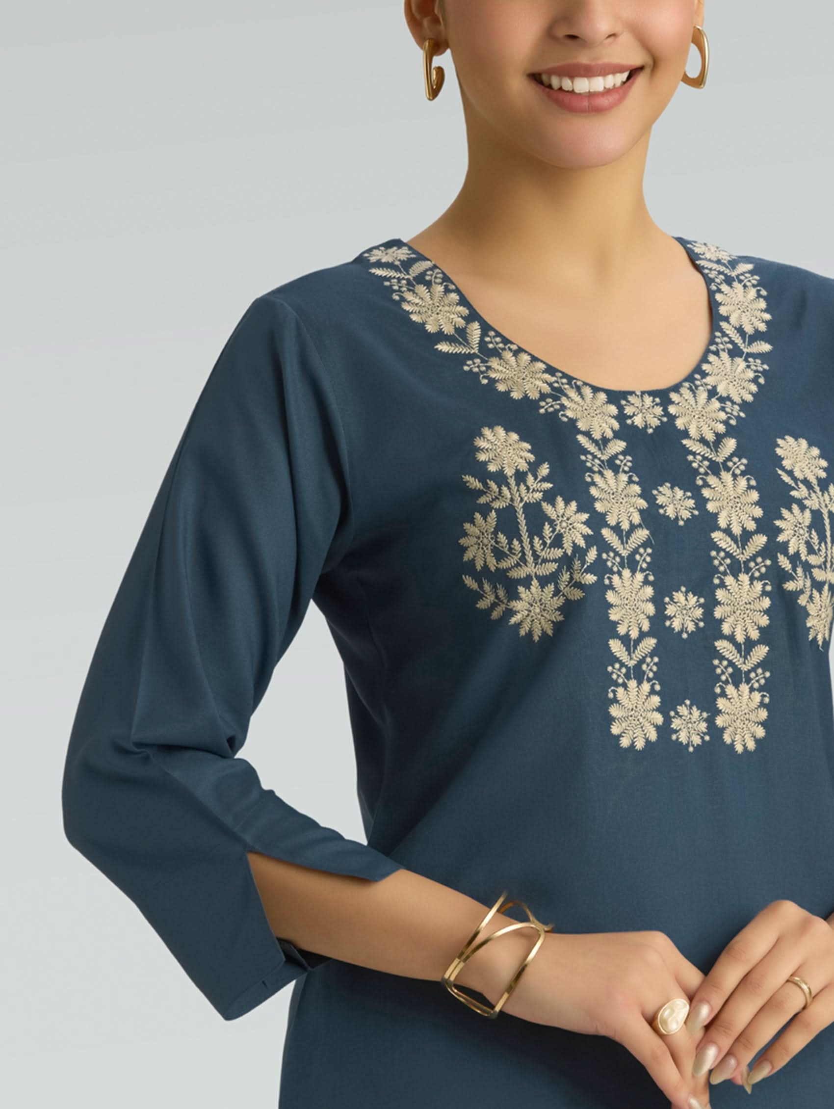 Woman wearing a blue dress with floral embroidery on a gray background