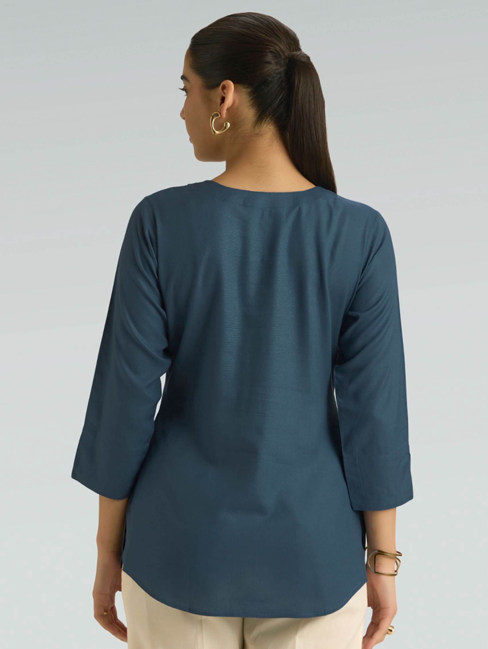 Woman wearing a blue top with 3/4 sleeves on a gray background