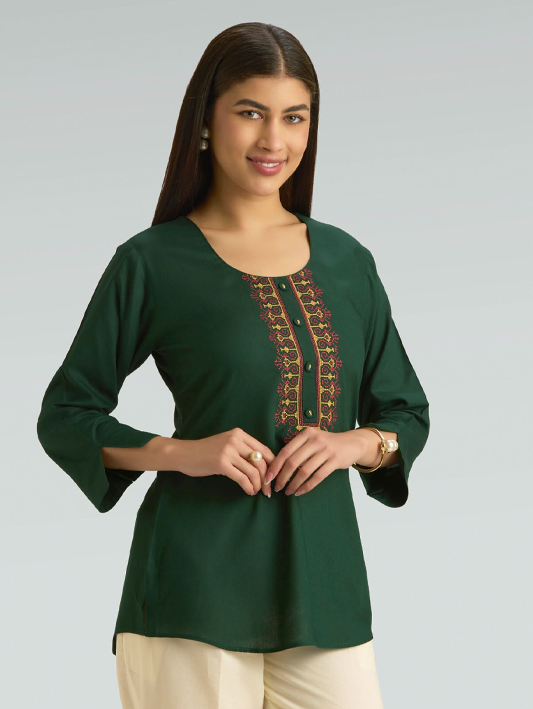 Woman wearing a green top with embroidery on a gray background