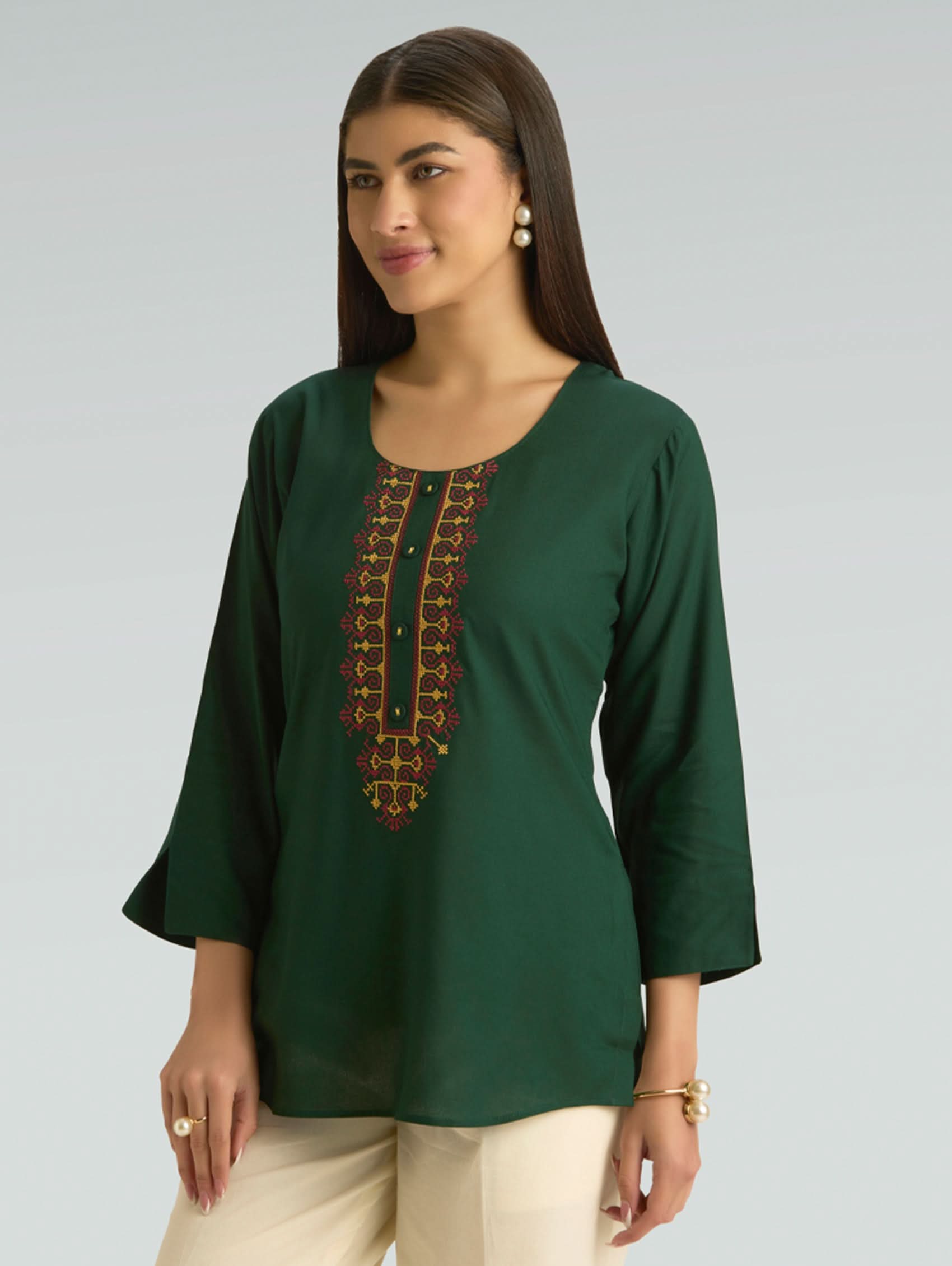 Woman wearing a green top with embroidery on a gray background