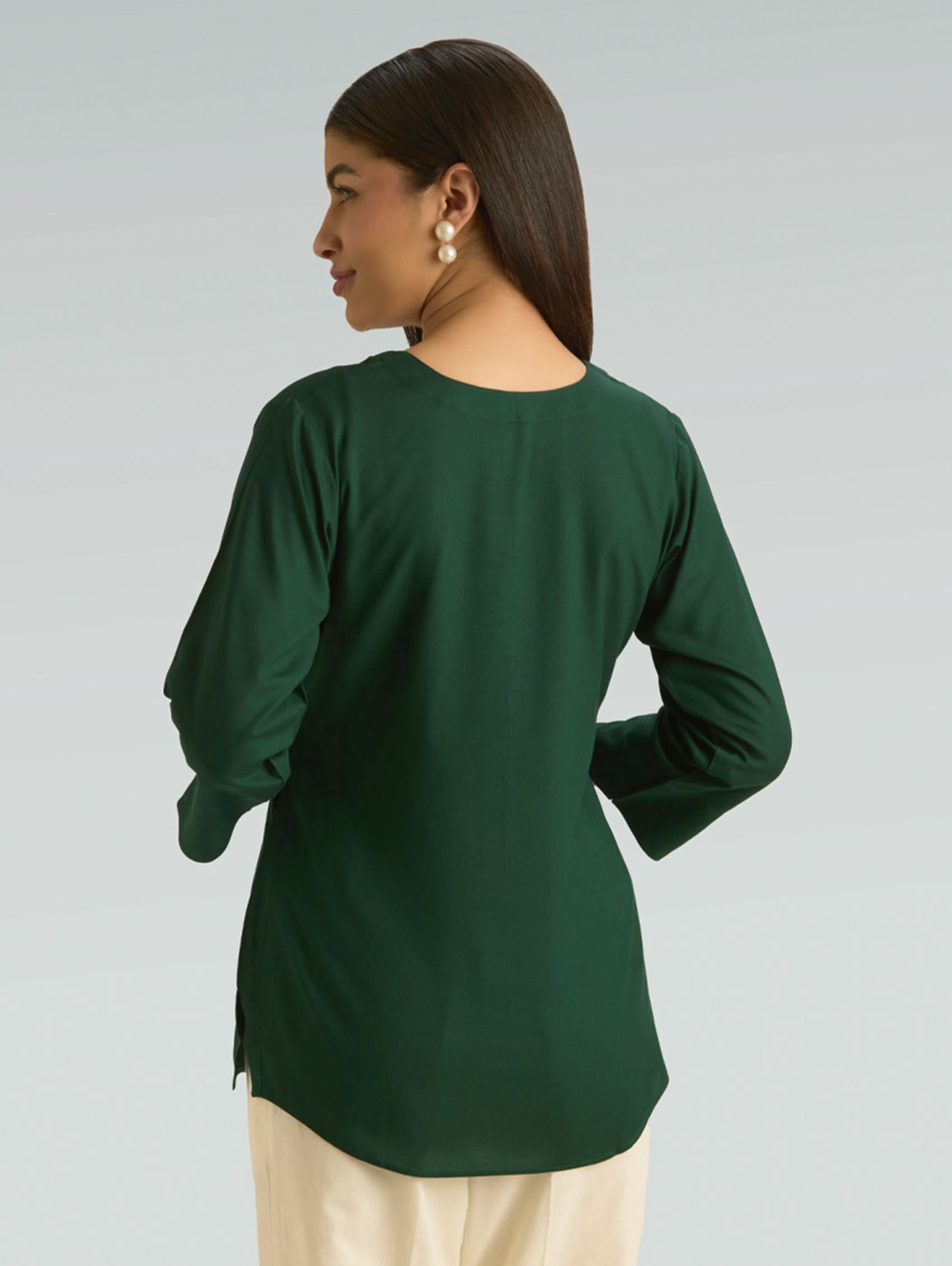 Woman wearing a green long-sleeve top against a gray background