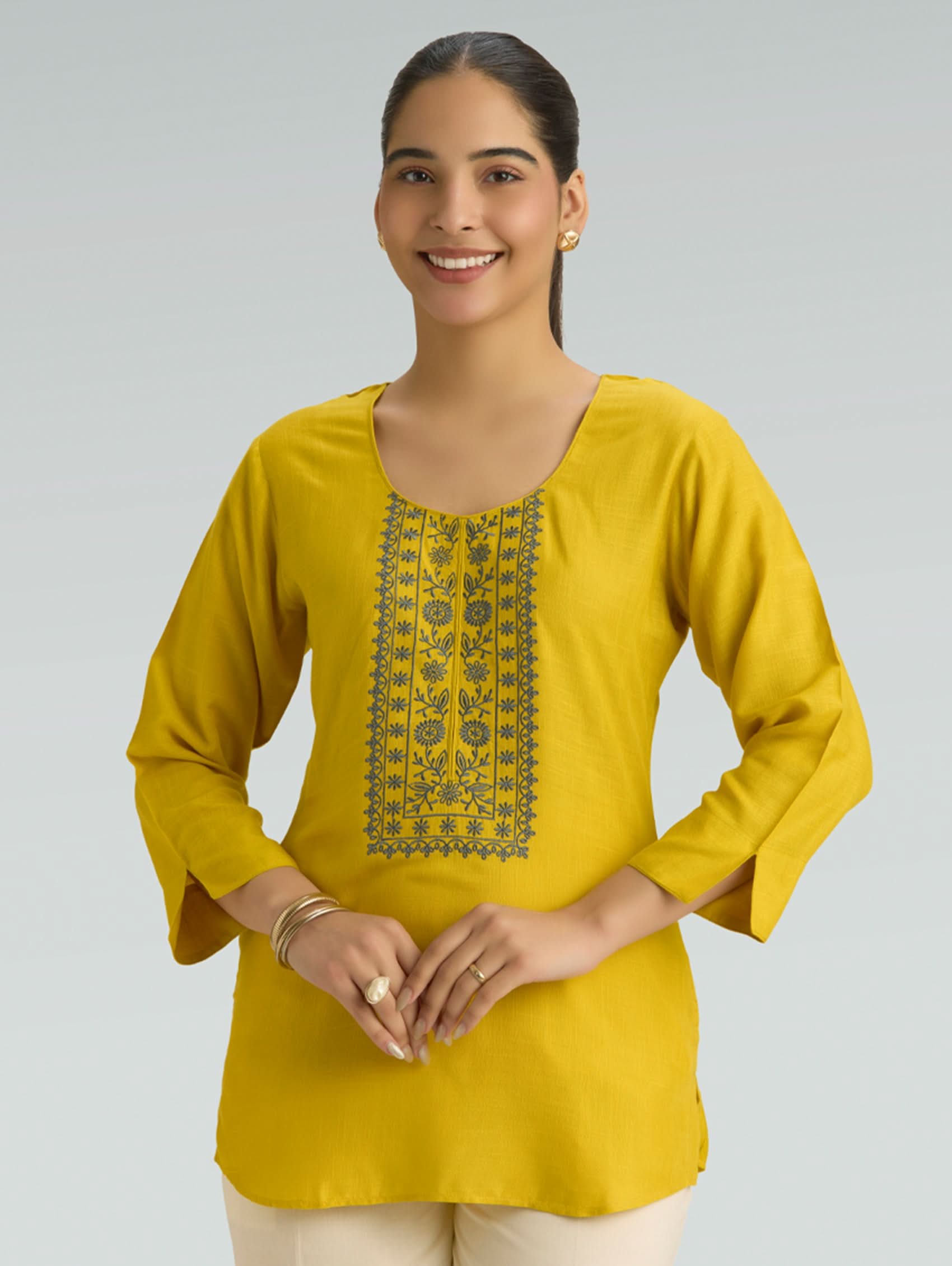 Woman wearing a yellow kurta with floral embroidery on a gray background