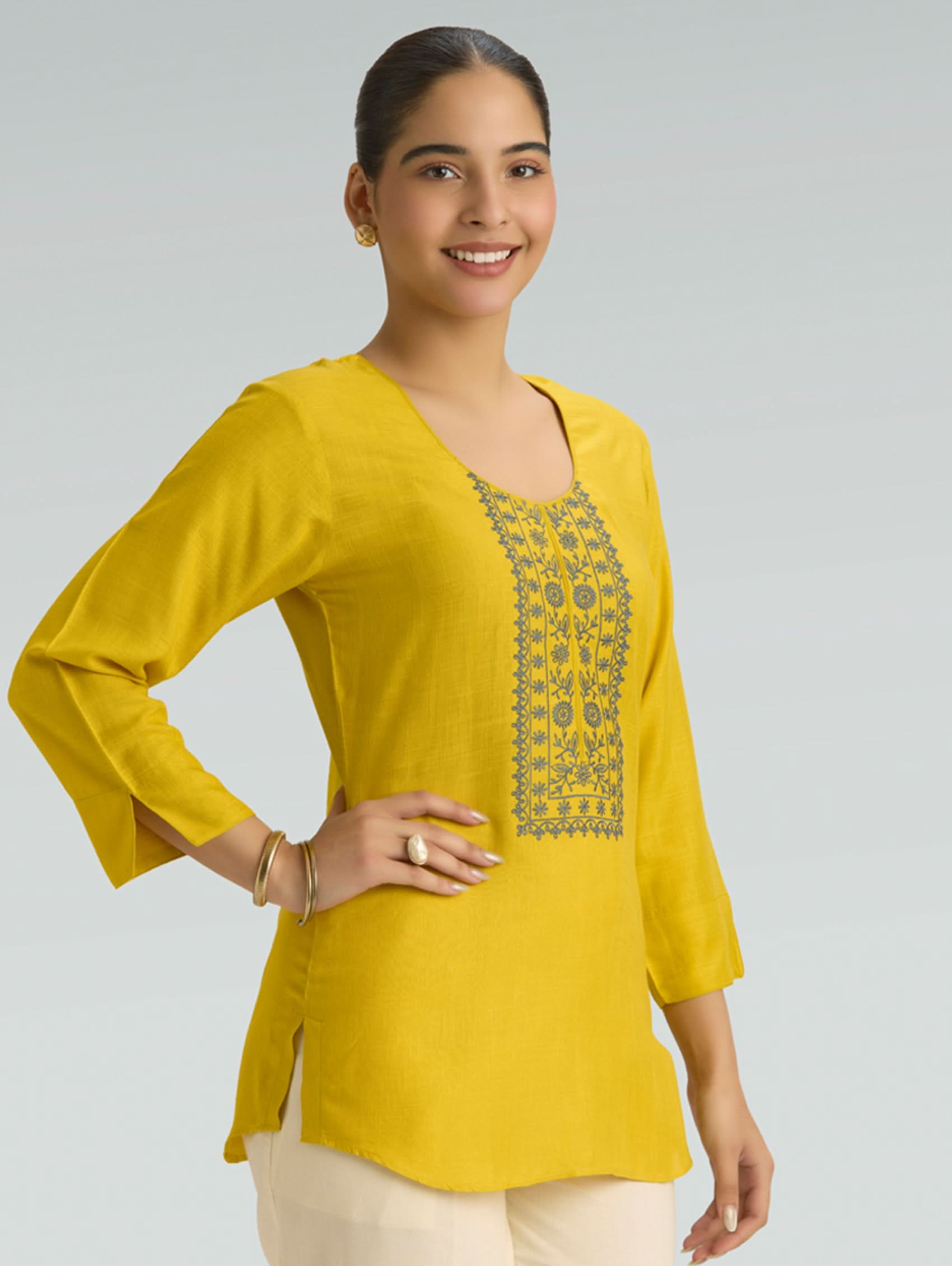 Woman wearing a yellow top with intricate embroidery on a gray background