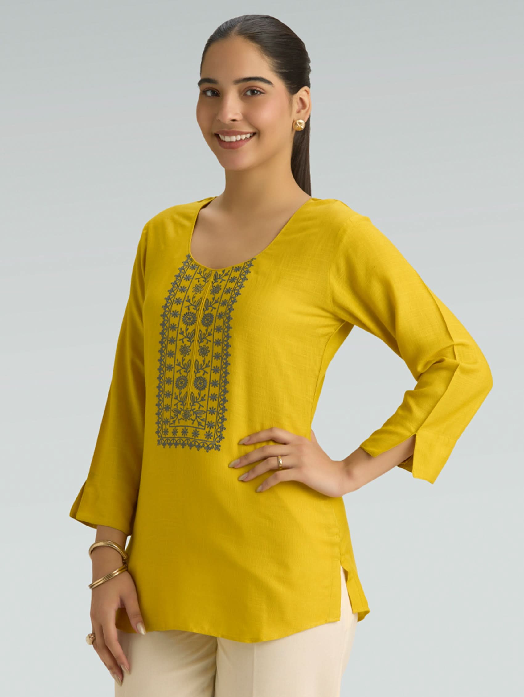 Woman wearing a yellow top with embroidery on a gray background