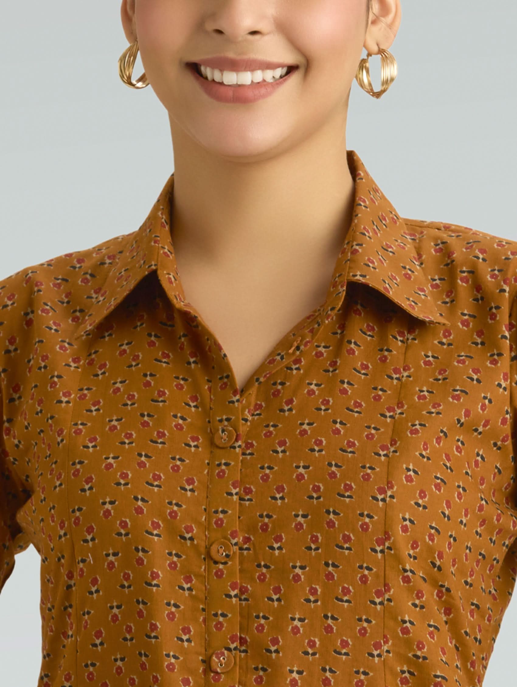 Woman wearing a mustard yellow floral shirt against a gray background