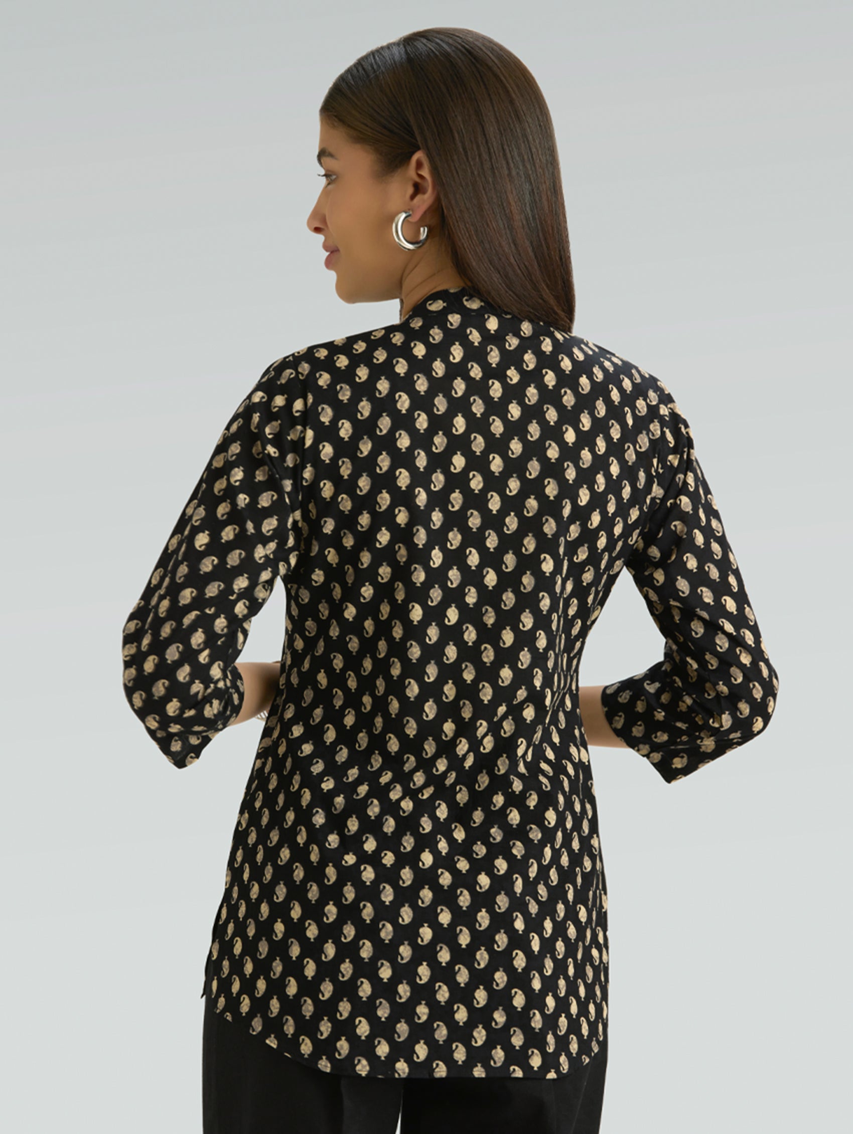 Woman wearing a black and beige patterned shirt against a gray background