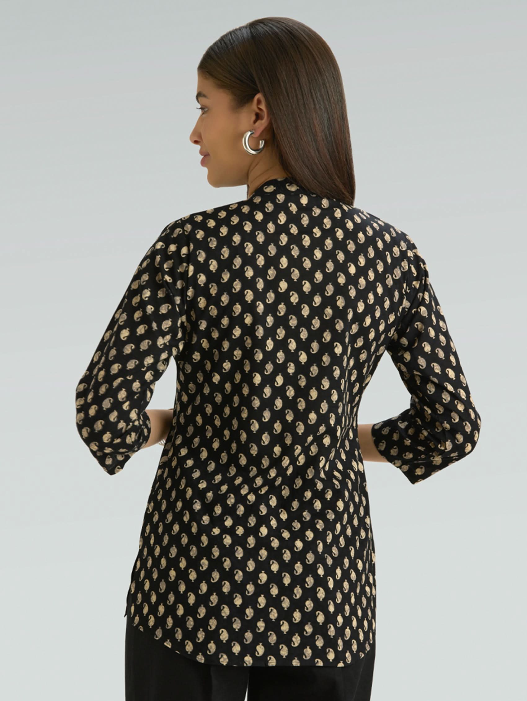 Woman wearing a black and beige patterned shirt against a gray background