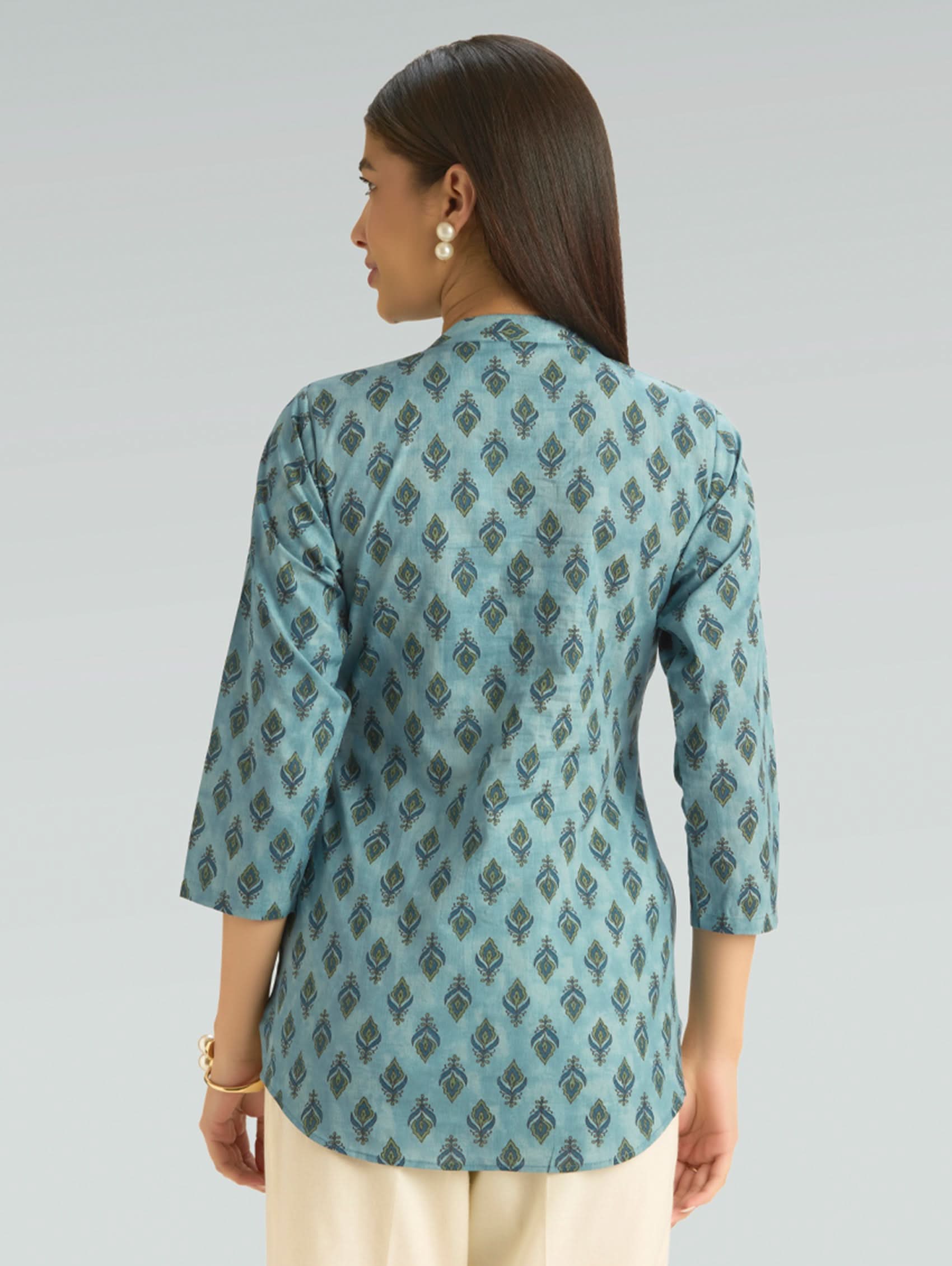Woman wearing a teal patterned top against a gray background