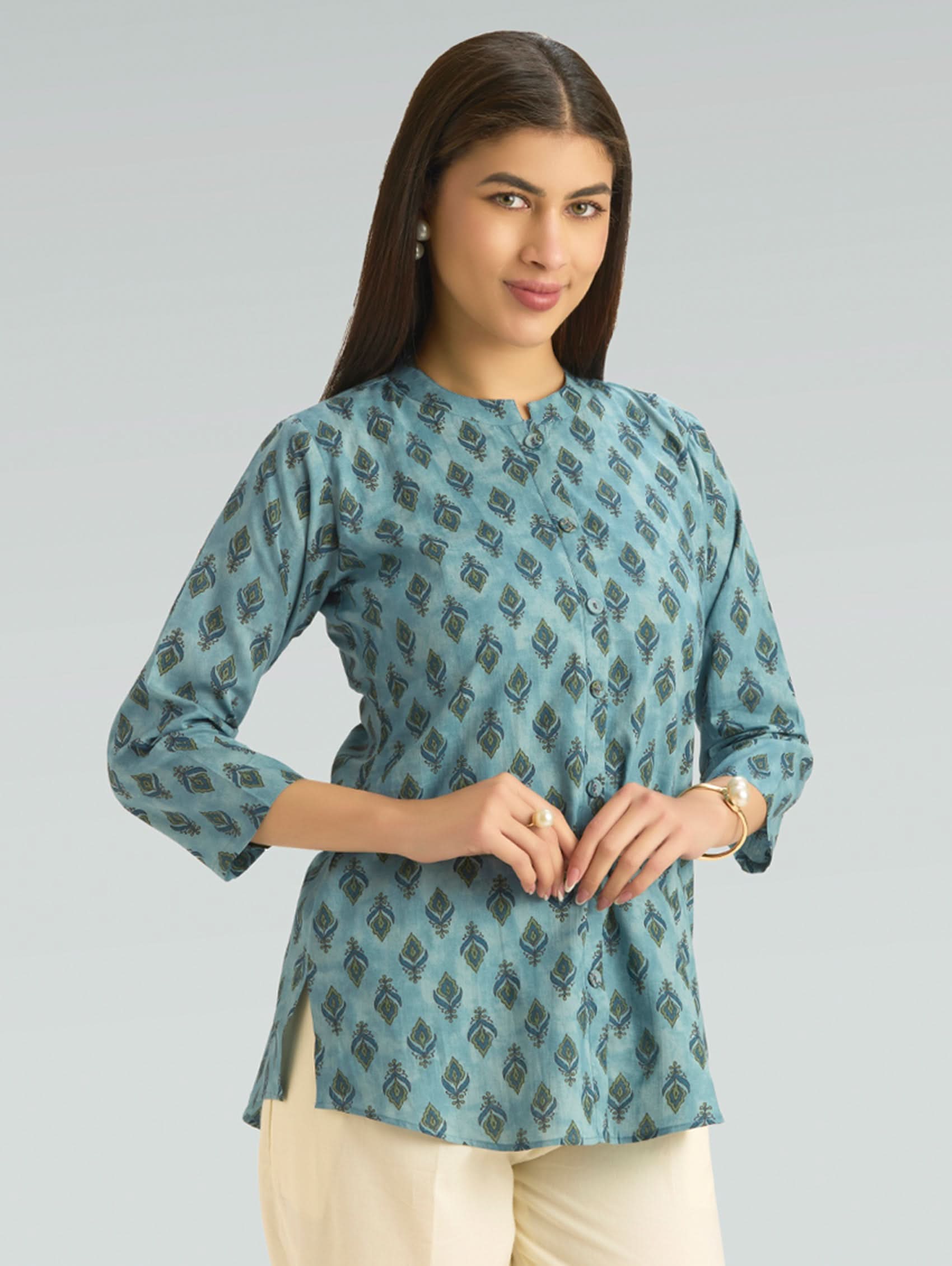 Woman wearing a teal patterned top against a gray background
