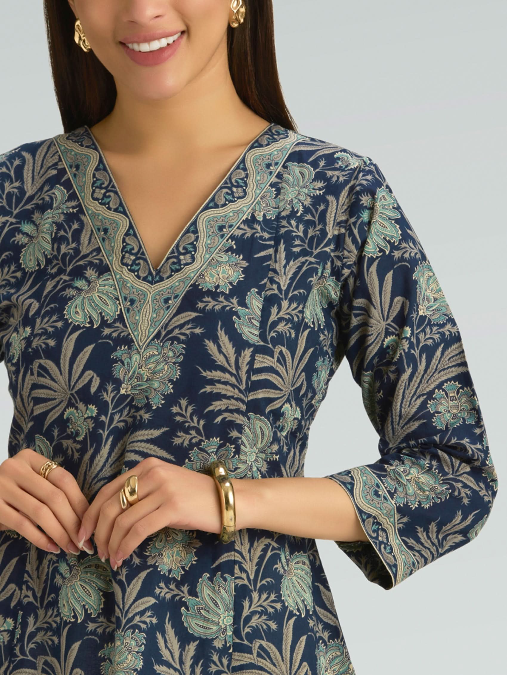 Woman wearing a navy blue floral patterned dress with gold jewelry on a gray background