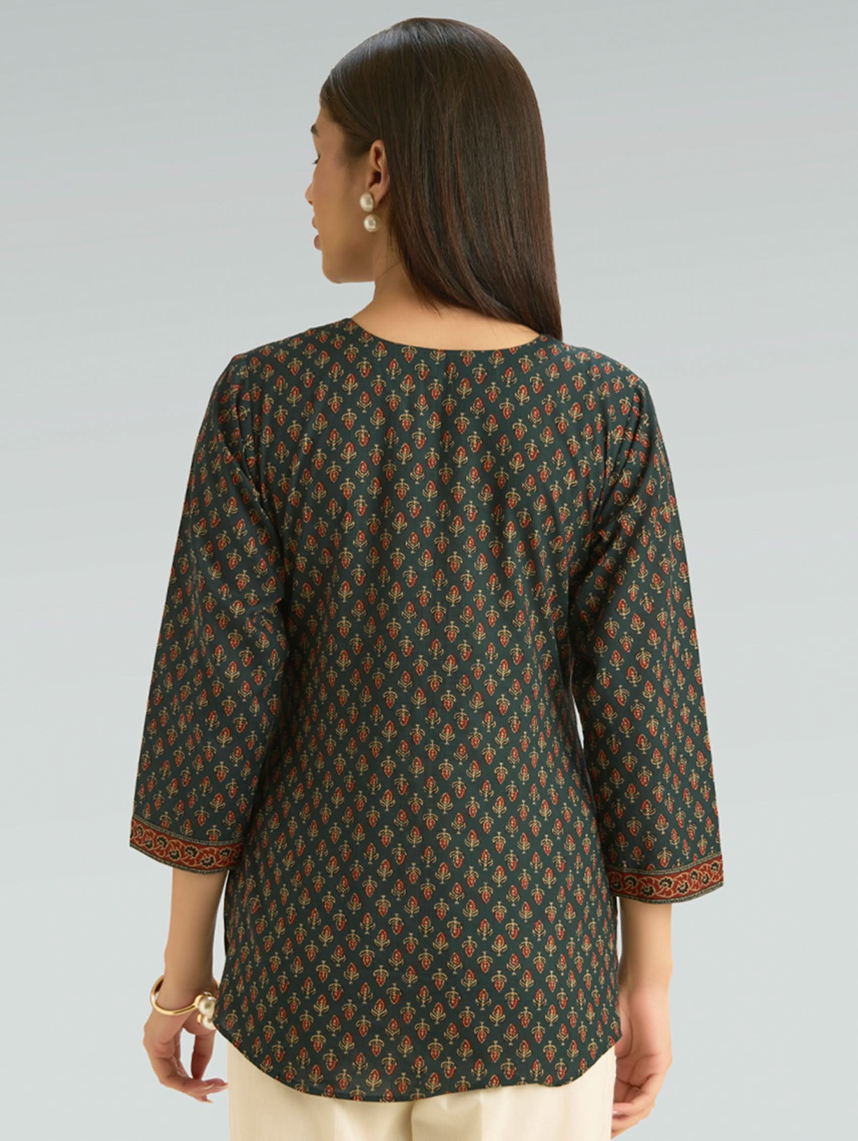 Woman wearing a patterned green and brown top on a gray background