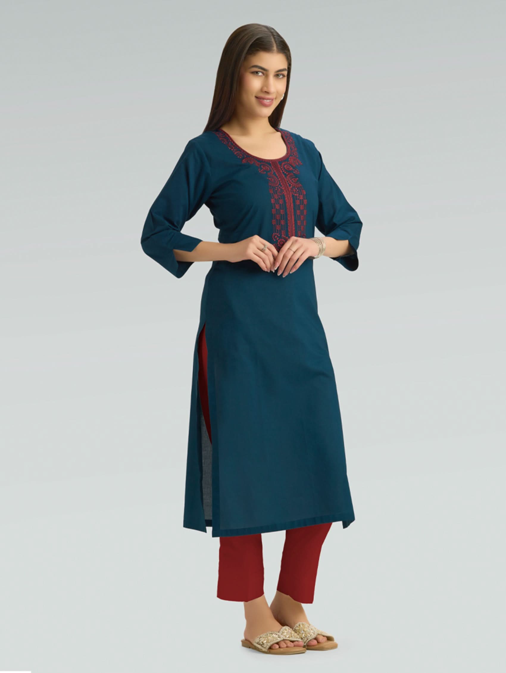 Woman wearing a teal kurta with red embroidery on a gray background