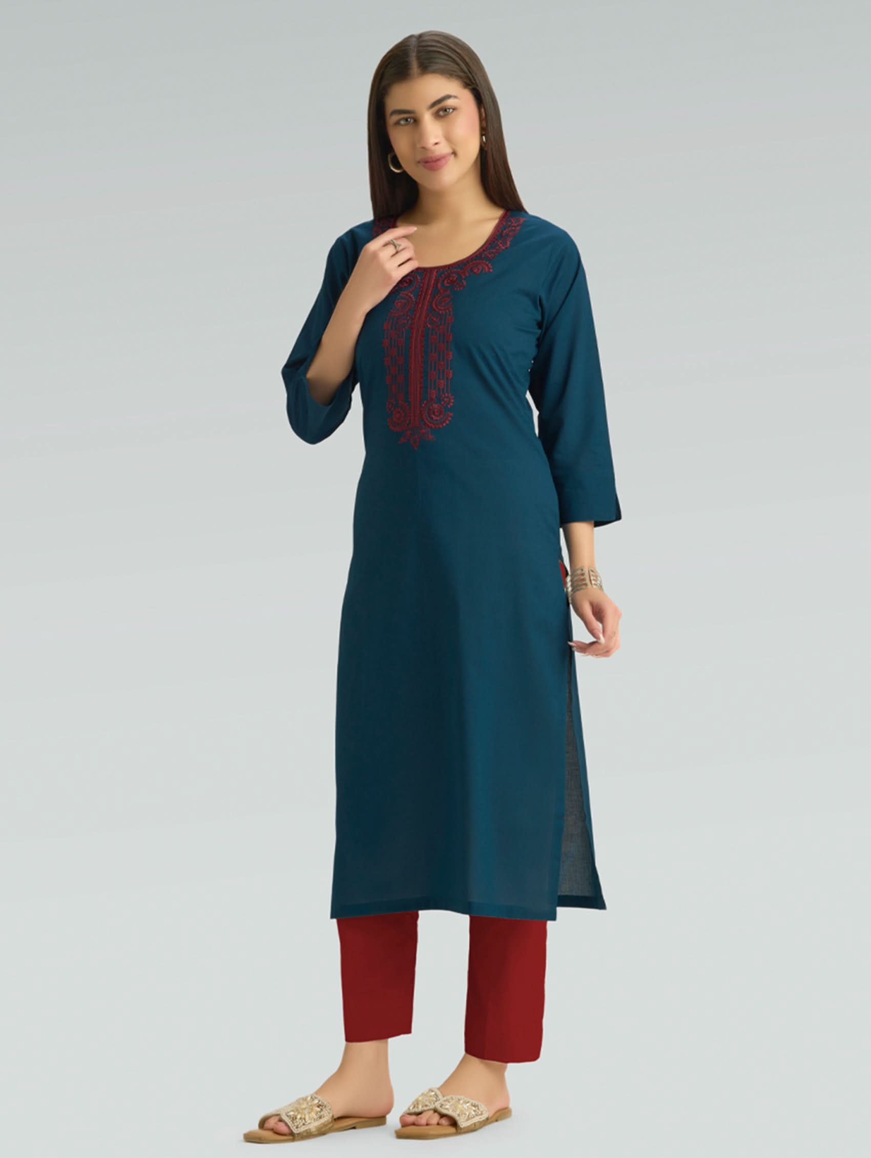 Woman wearing a teal kurta with red embroidery and red pants on a light gray background