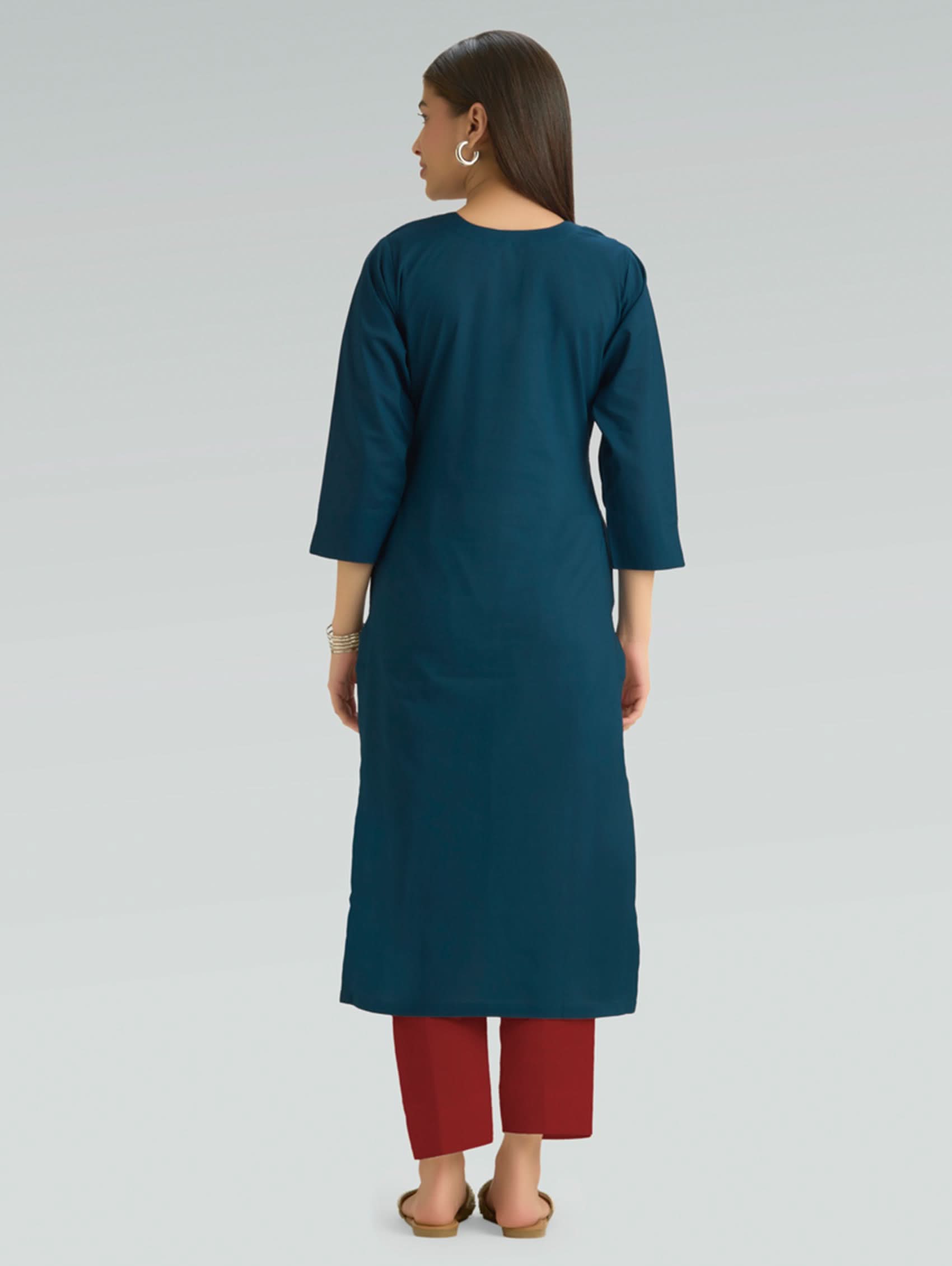 A woman in a teal kurta paired with red pants, shown in a back pose against a gray background.