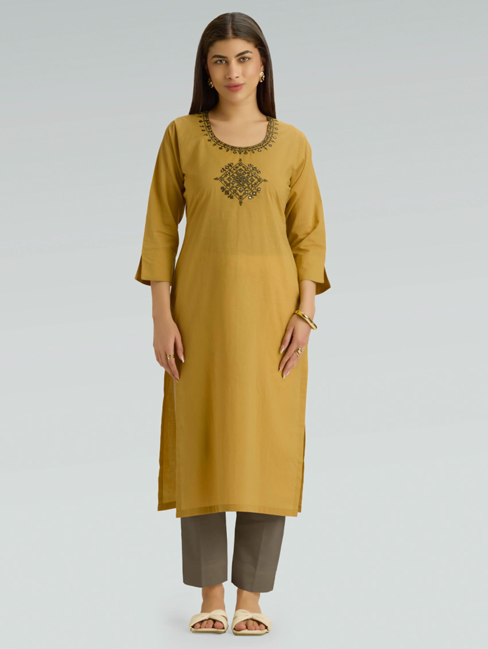 Woman wearing a mustard yellow kurta with embroidery on a gray background