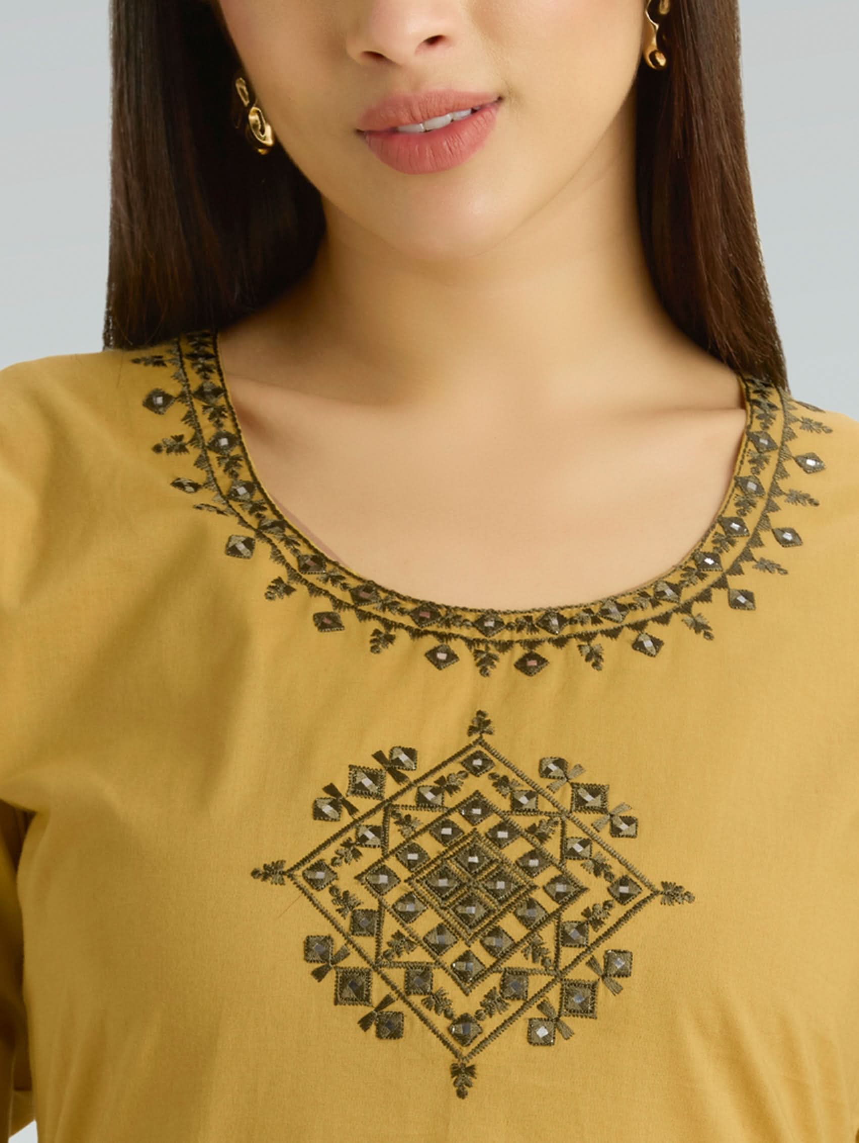 Close-up of a mustard yellow top with intricate black embroidery on a plain background