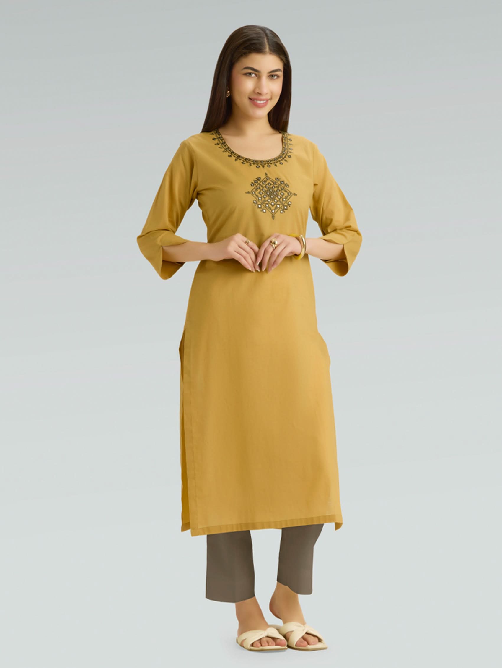 Woman wearing a mustard yellow kurta with embroidery on a gray background
