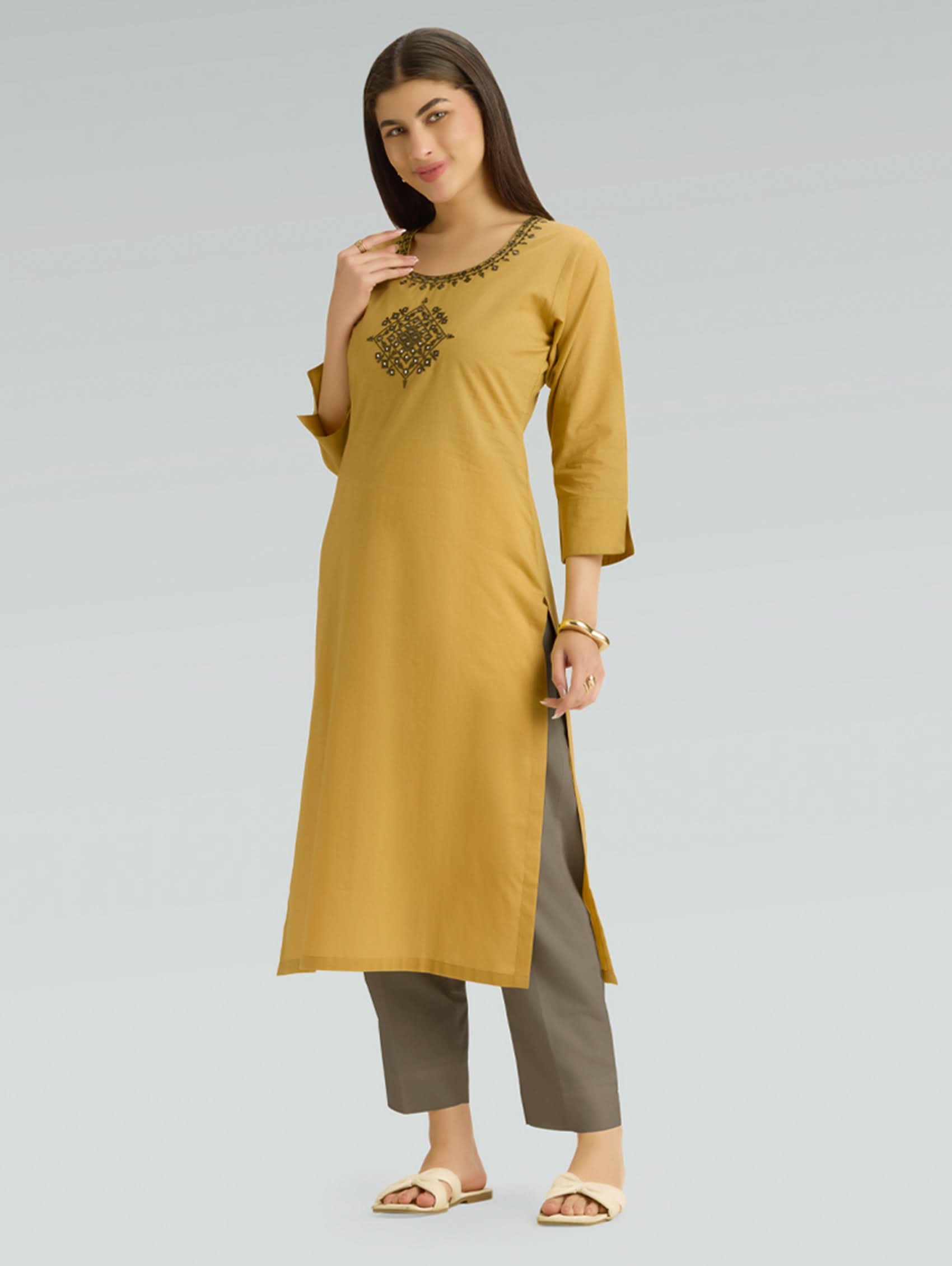Woman wearing a mustard yellow kurta with brown pants on a light gray background