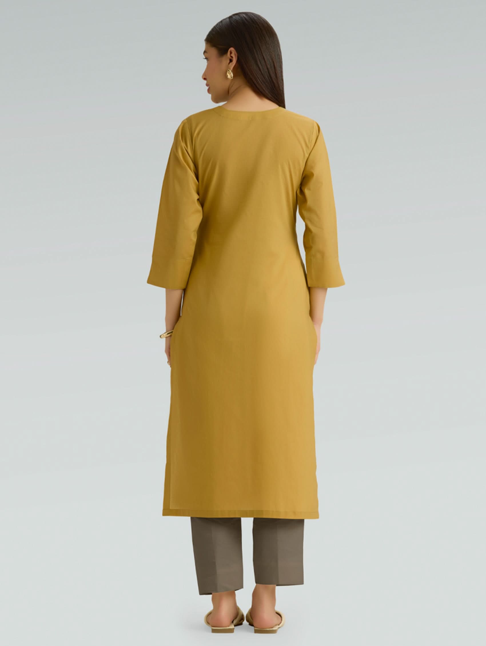 Woman wearing a mustard yellow kurta with brown pants on a light gray background