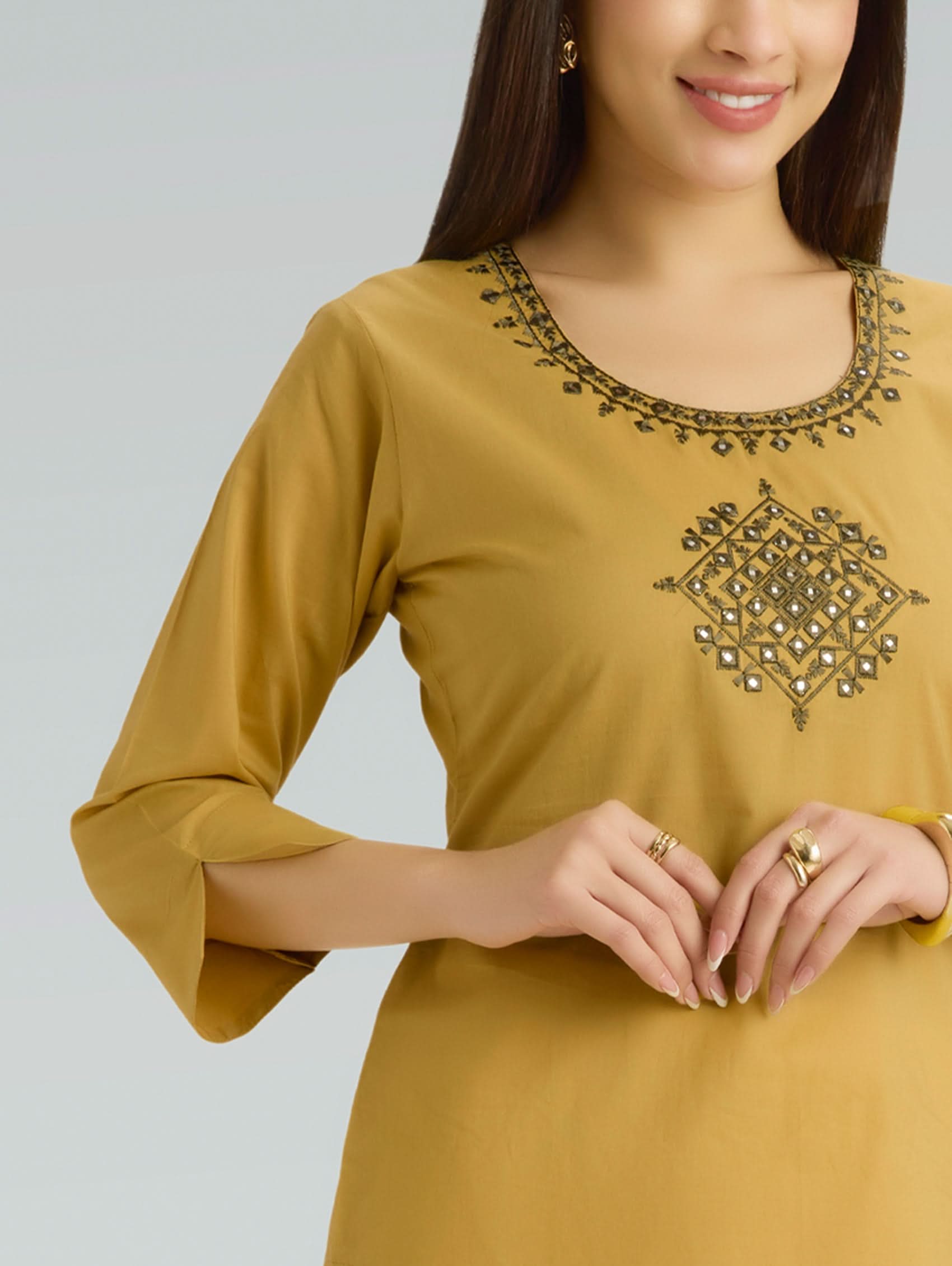 Woman wearing a mustard yellow kurta with intricate black embroidery on a plain background
