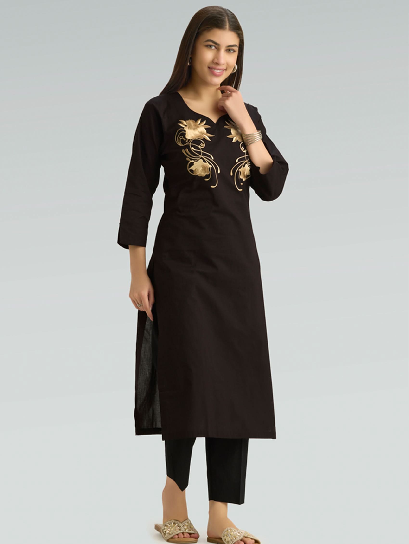 Woman wearing a black kurta with gold embroidery on a gray background