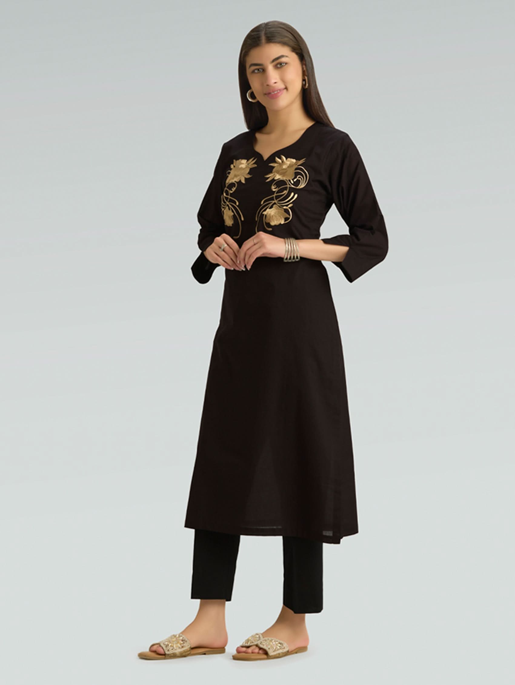 Woman wearing a black kurta with gold embroidery on a gray background