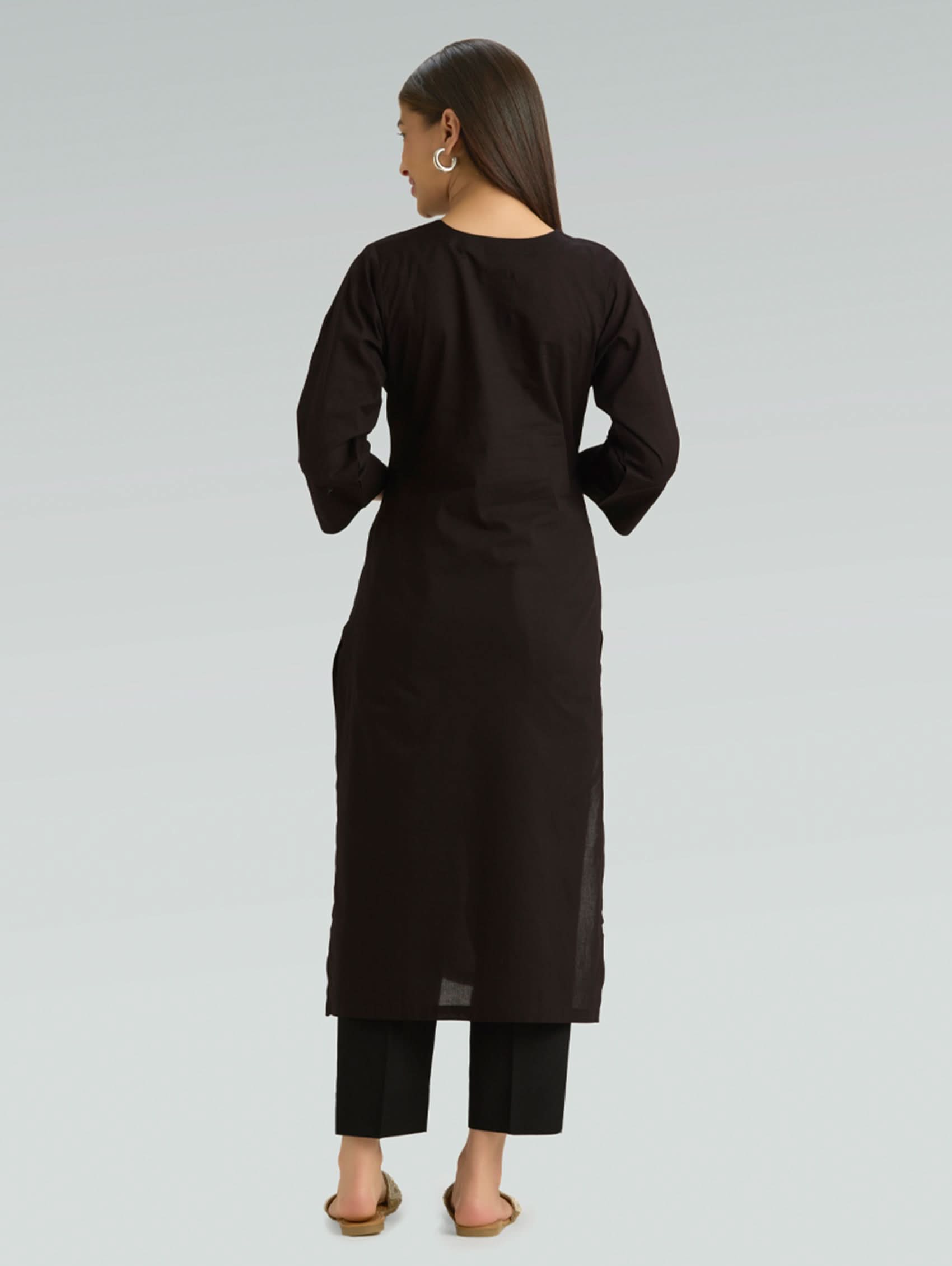 Woman wearing a black long-sleeve top and pants on a gray background