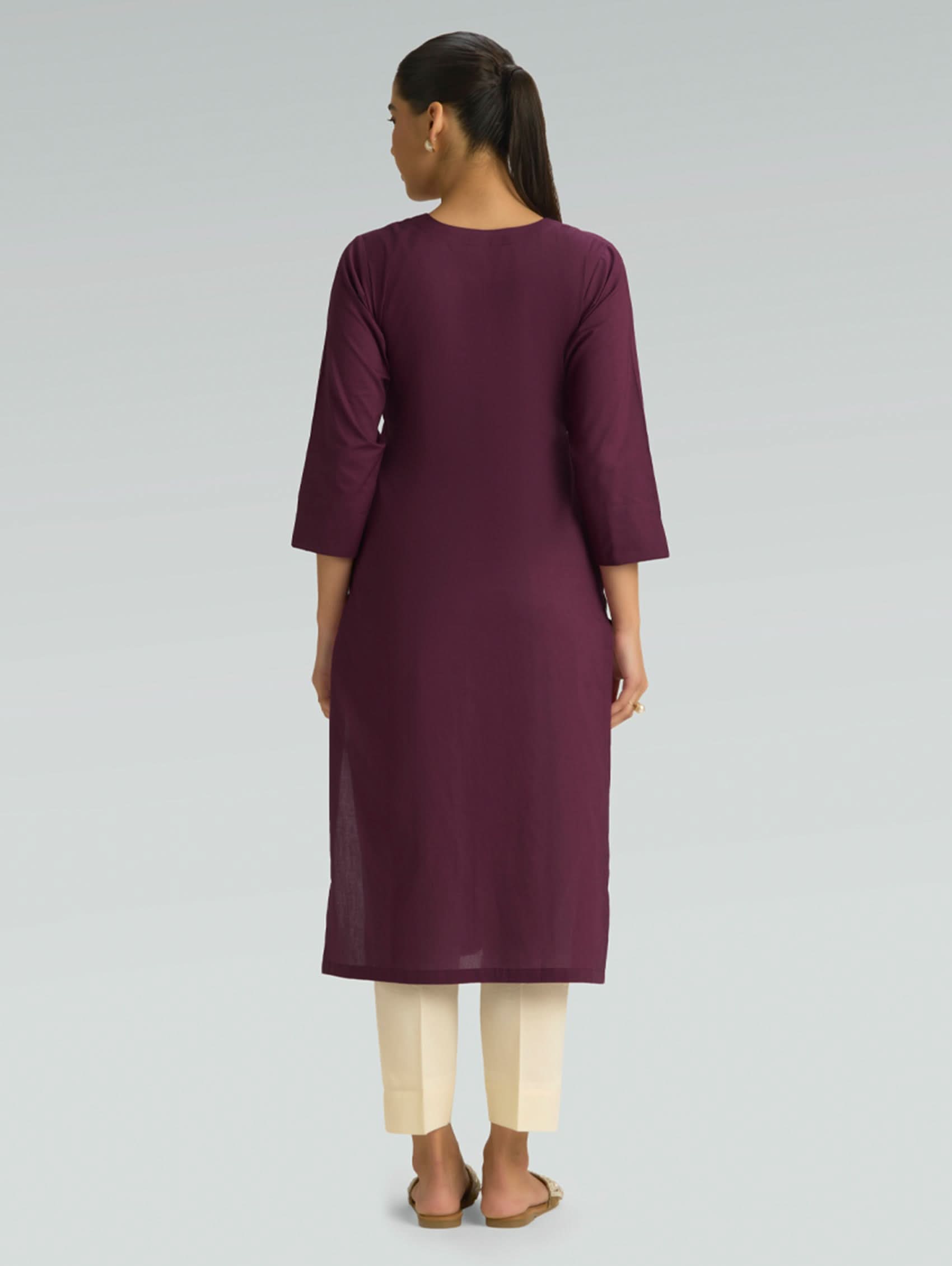 A woman in a purple kurta paired with beige pants, shown in a back pose against a light gray background.