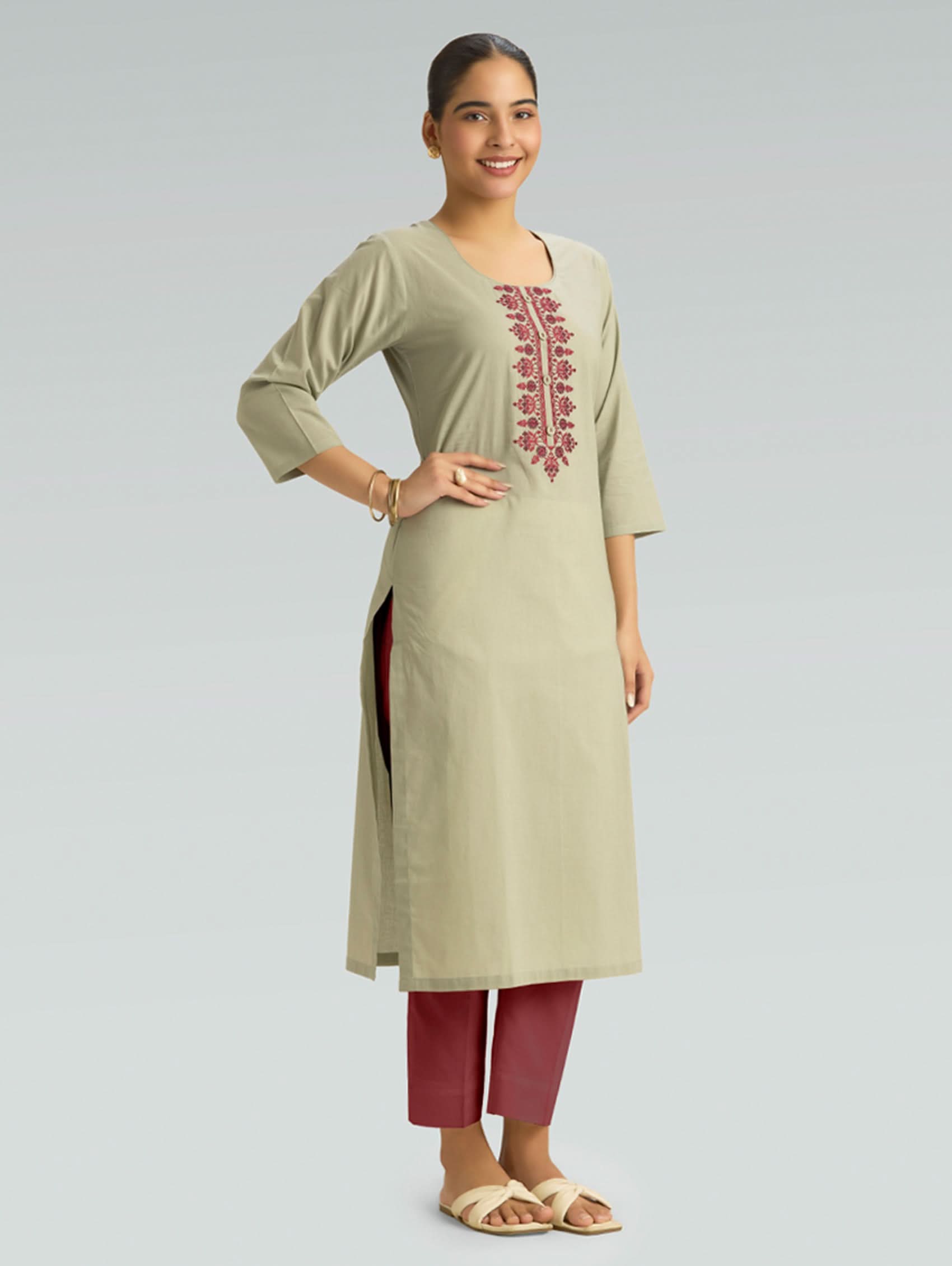 A woman wearing a straight-fit beige kurta with a round neckline, adorned with red embroidery, set against a light gray background.