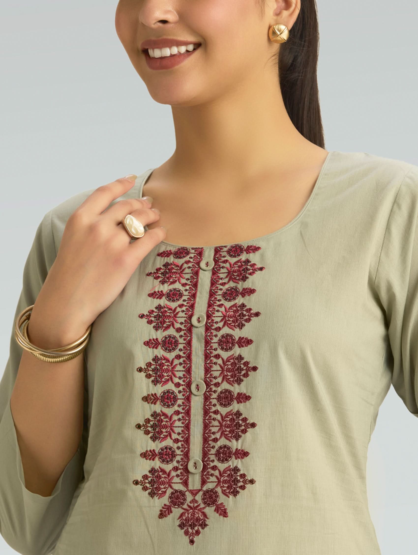Woman wearing a light green kurta with red embroidery on a plain background