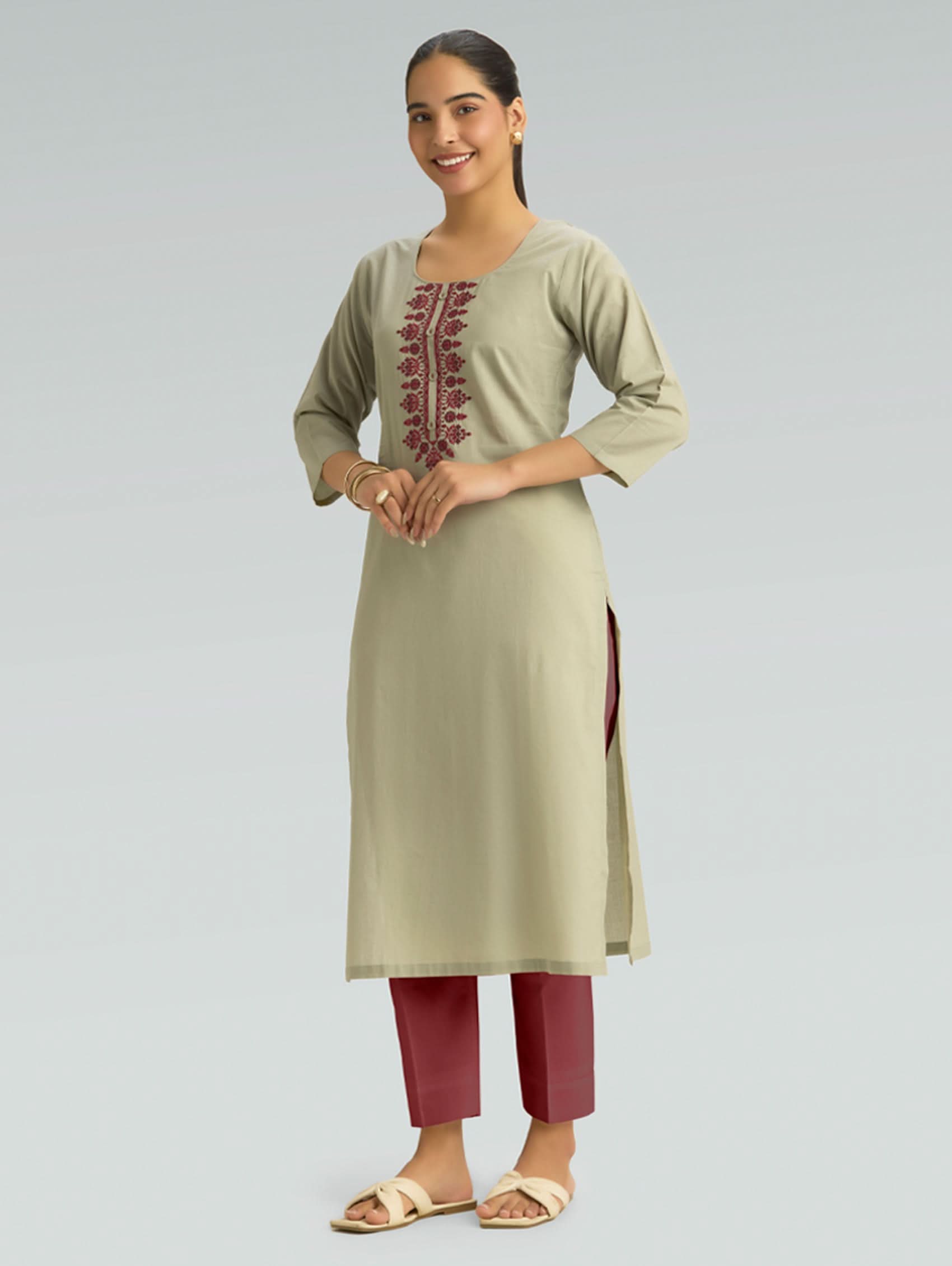 Woman wearing a light green kurta with maroon embroidery and red pants on a gray background
