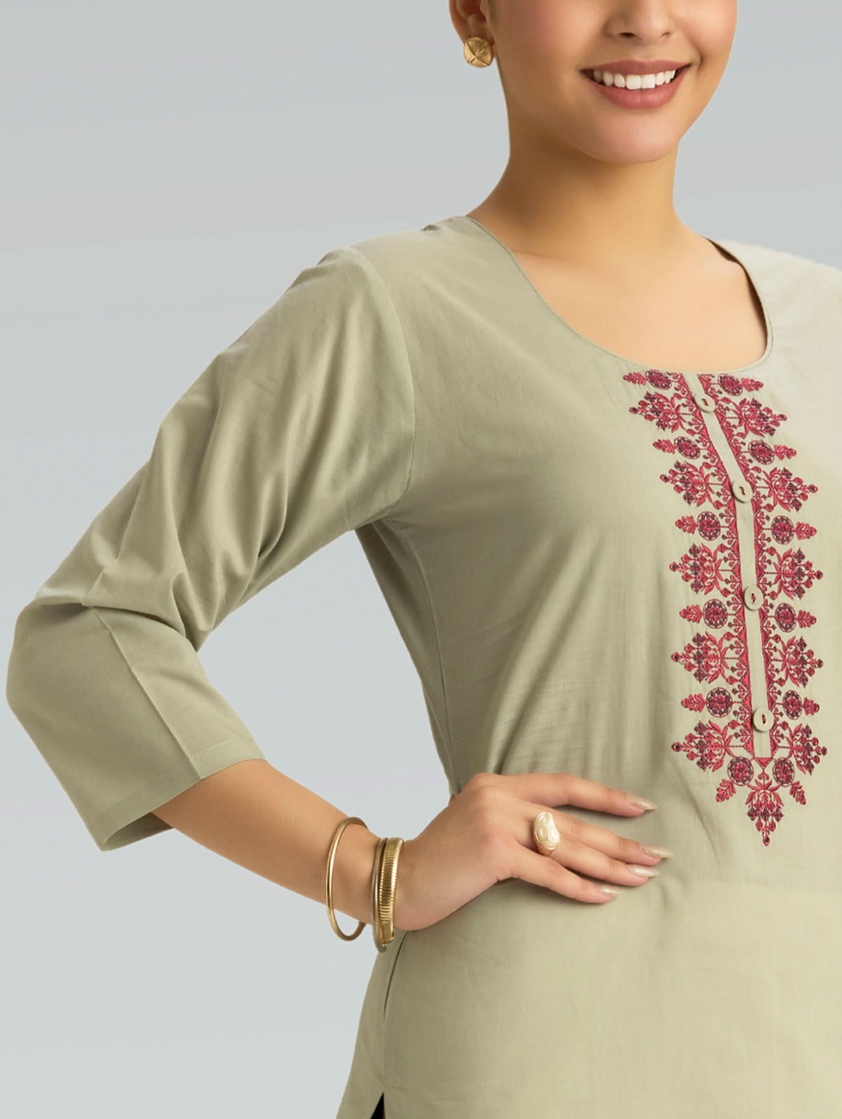 Woman wearing a light green kurta with pink embroidery on a plain background