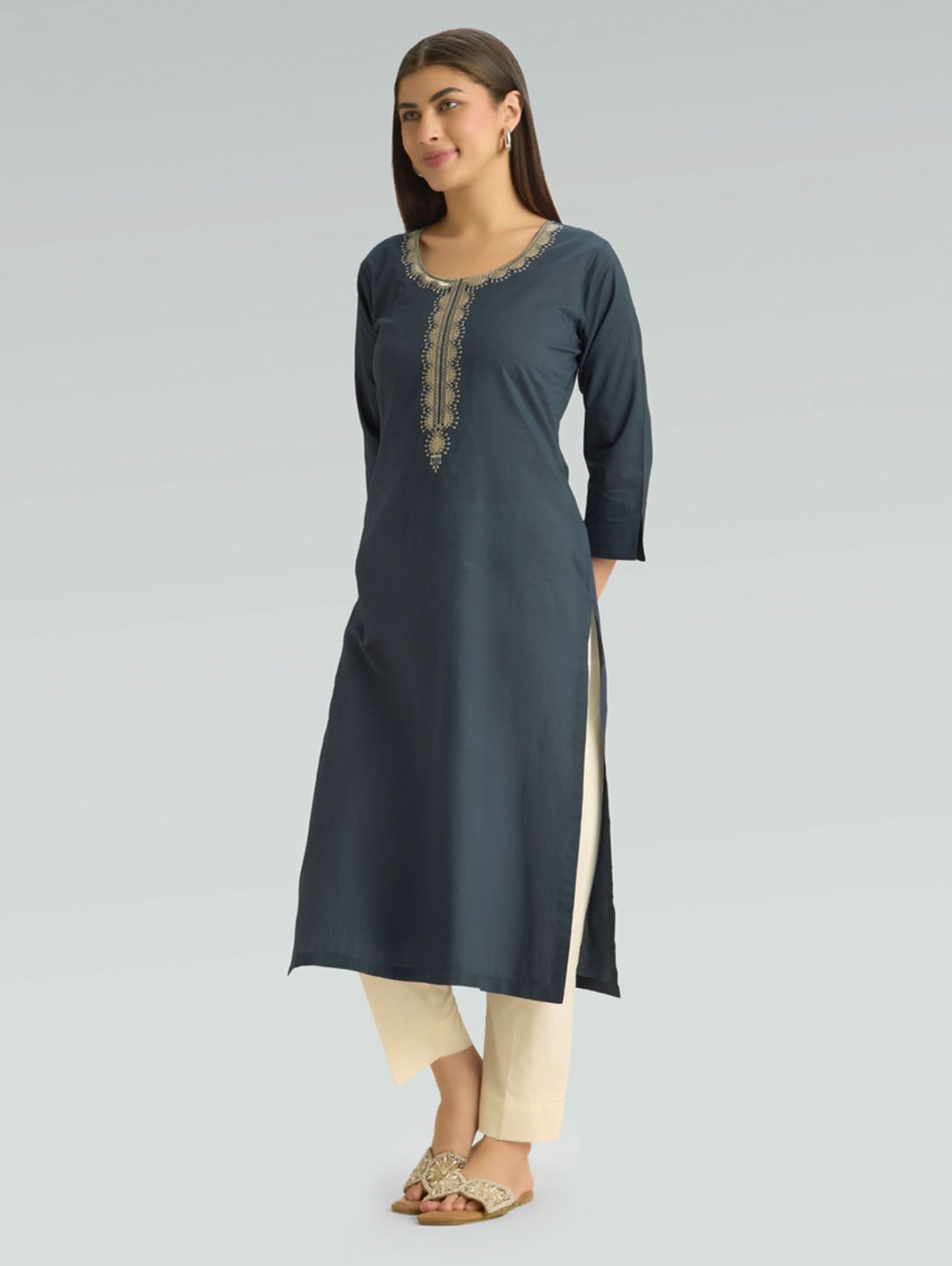 Woman wearing a dark gray kurta with beige pants on a light gray background